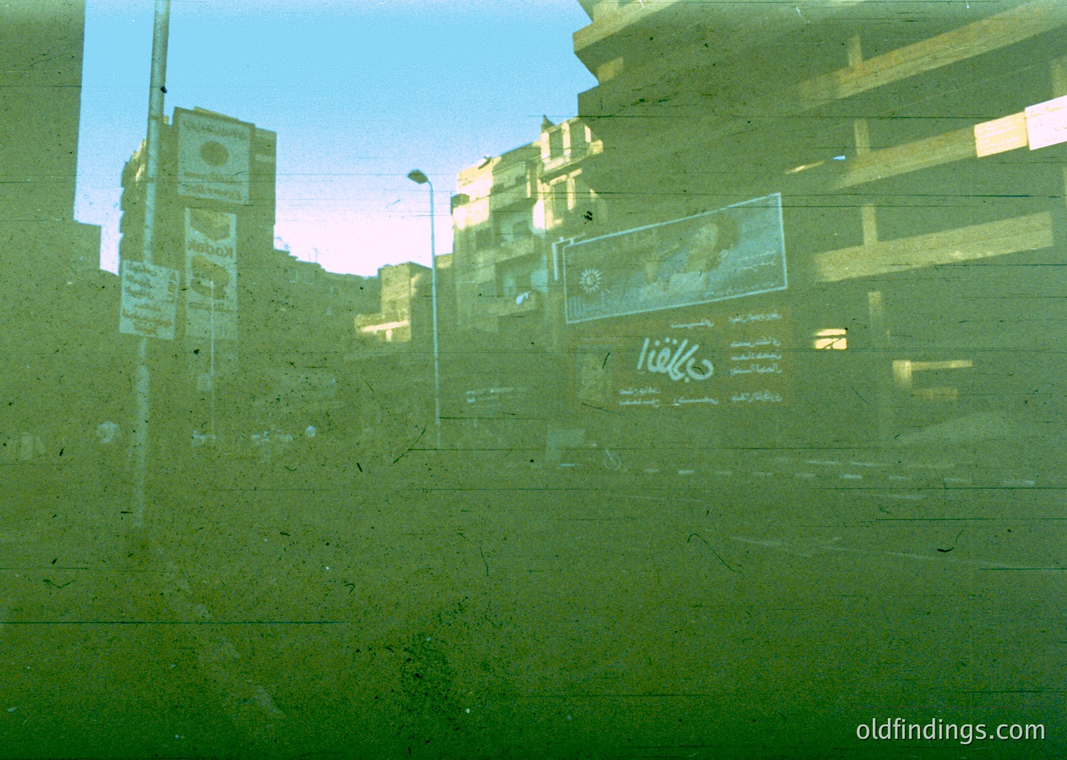 Reflection of urban street scene through a fogged or scratched window. Visible: faded billboards (Pepsi, Arabic script), multi-story concrete buildings, and a streetlight. Likely Middle Eastern city, 1980s–1990s era.