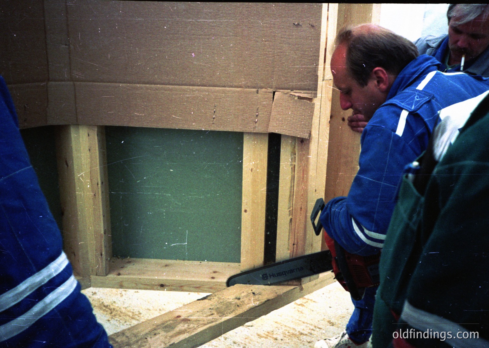 Construction workers in blue uniforms with reflective stripes examine a framed window opening in a partially built wooden structure. The scene suggests mid-construction, likely residential or light commercial.