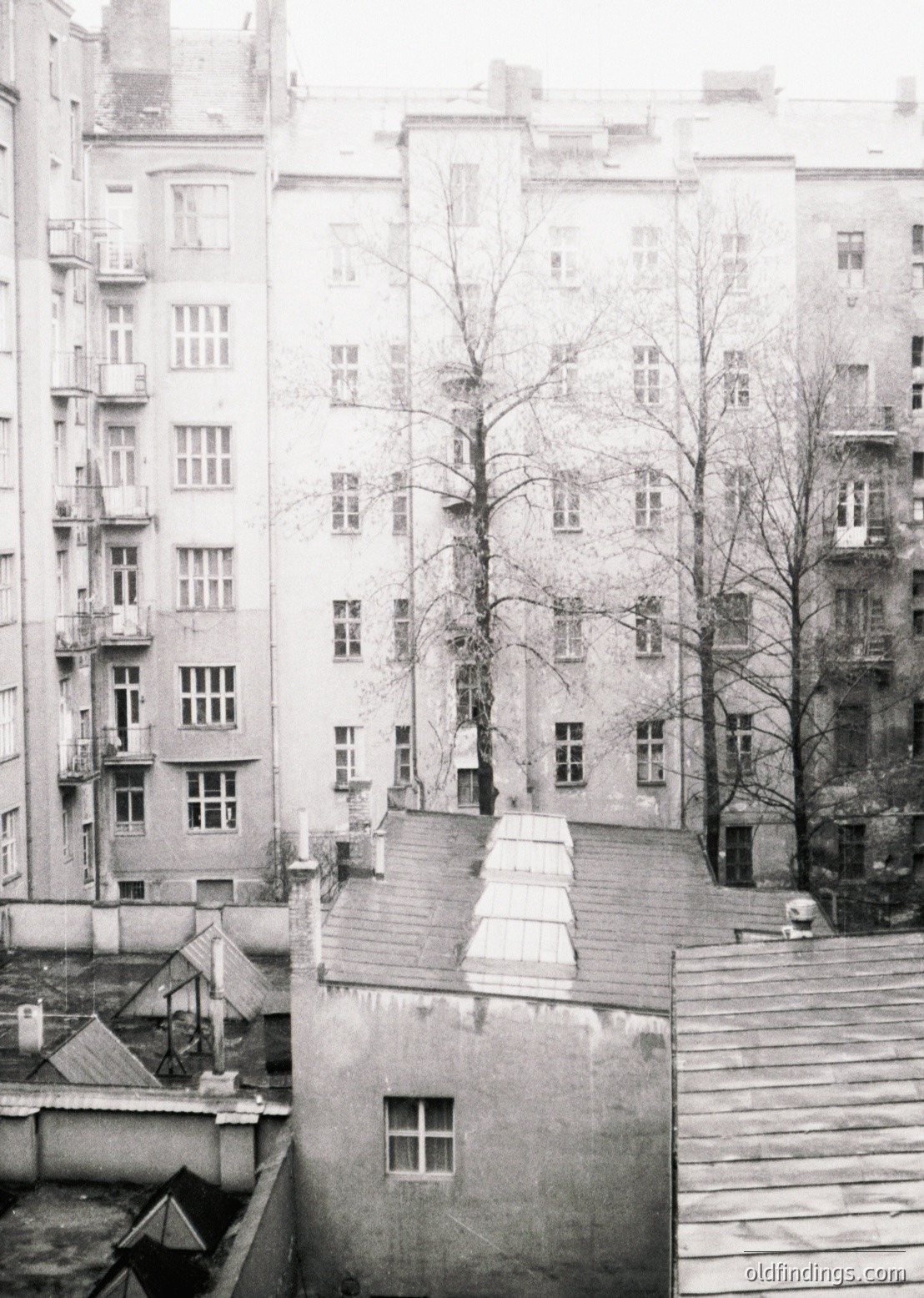 Mid-century Soviet-era apartment block with symmetrical, utilitarian design—symmetrical windows, flat roofs, and narrow balconies. Bare winter trees frame a courtyard staircase leading to upper floors. Likely Eastern Europe, 1960s–1980s.