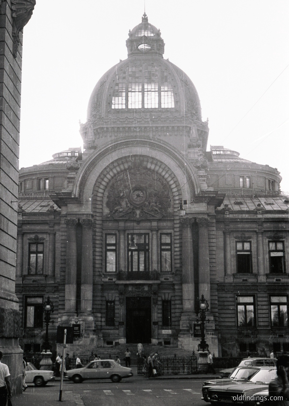 Neoclassical stone building with domed roof and grand arched entrance, featuring Soviet-era emblem above doorway. Mid-20th century urban street scene with vintage cars and pedestrians.