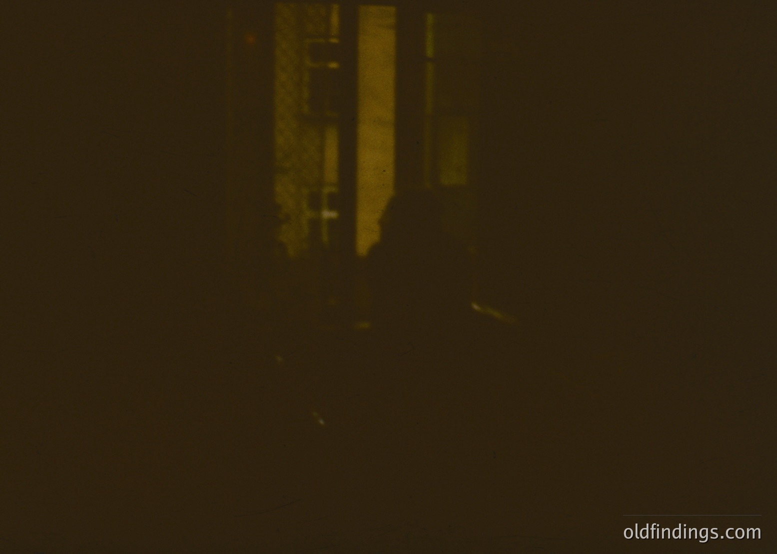 Low-light urban scene with minimal detail—blurred vertical structure (likely a building or pole) and faint horizontal lines suggesting a street or alley. Ambient lighting reveals minimal architectural context, possibly a cityscape or industrial area.