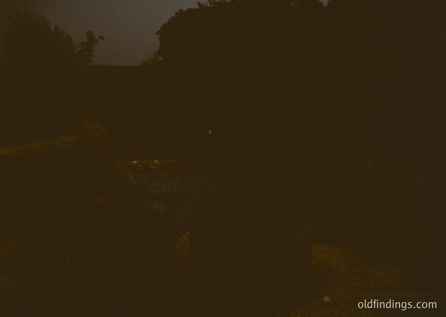 Low-light urban scene with faintly visible streetlights and indistinct architecture. Ambient glow suggests nighttime cityscape, possibly 20th century based on lighting style. Limited detail prevents precise location or era confirmation.