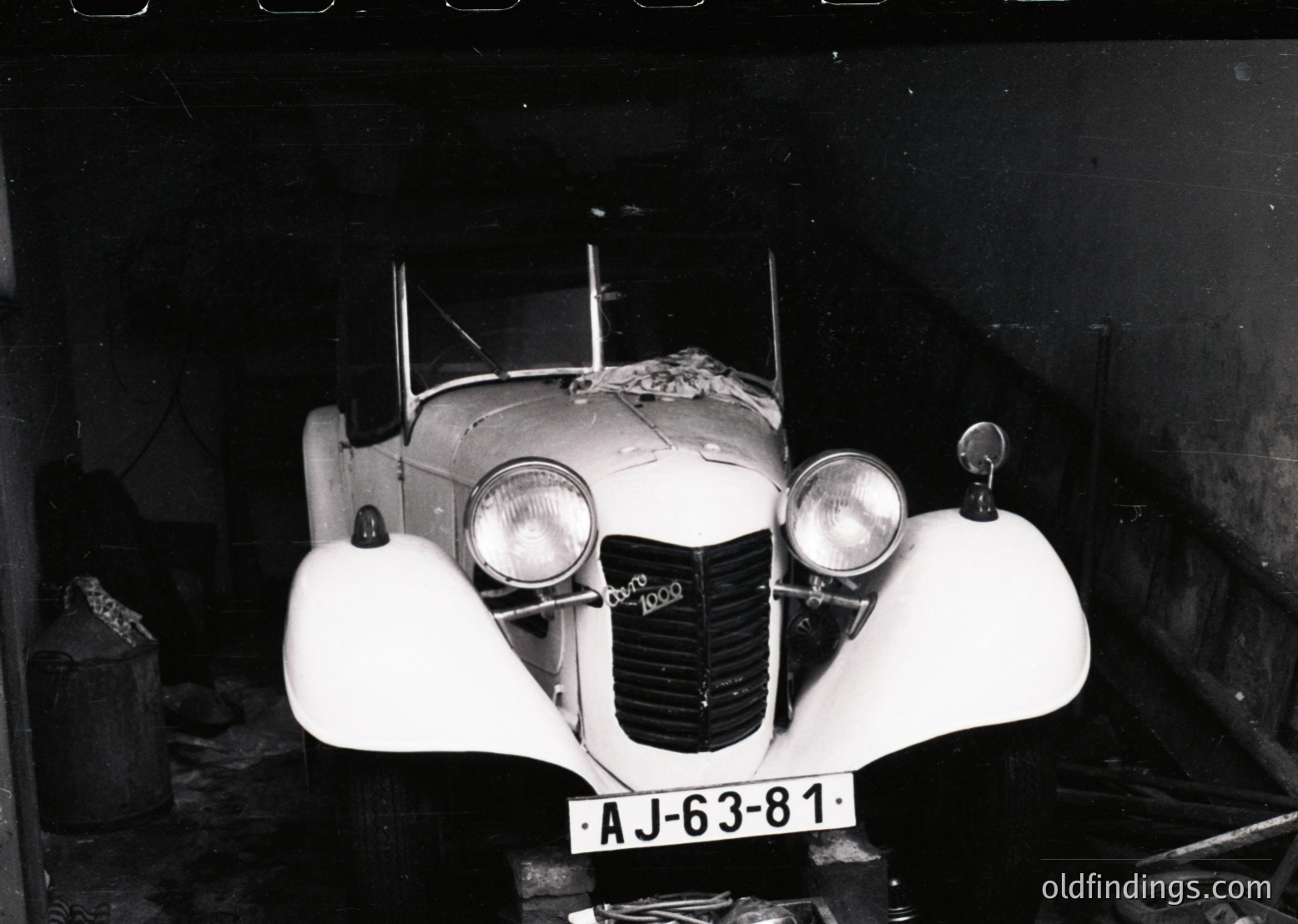 Classic 1930s-era roadster with streamlined bodywork, dual round headlights, and "AJ-63-81" license plate. Indoor setting suggests vintage automotive display or garage. Distinctive grille and chrome detailing highlight mid-century engineering.