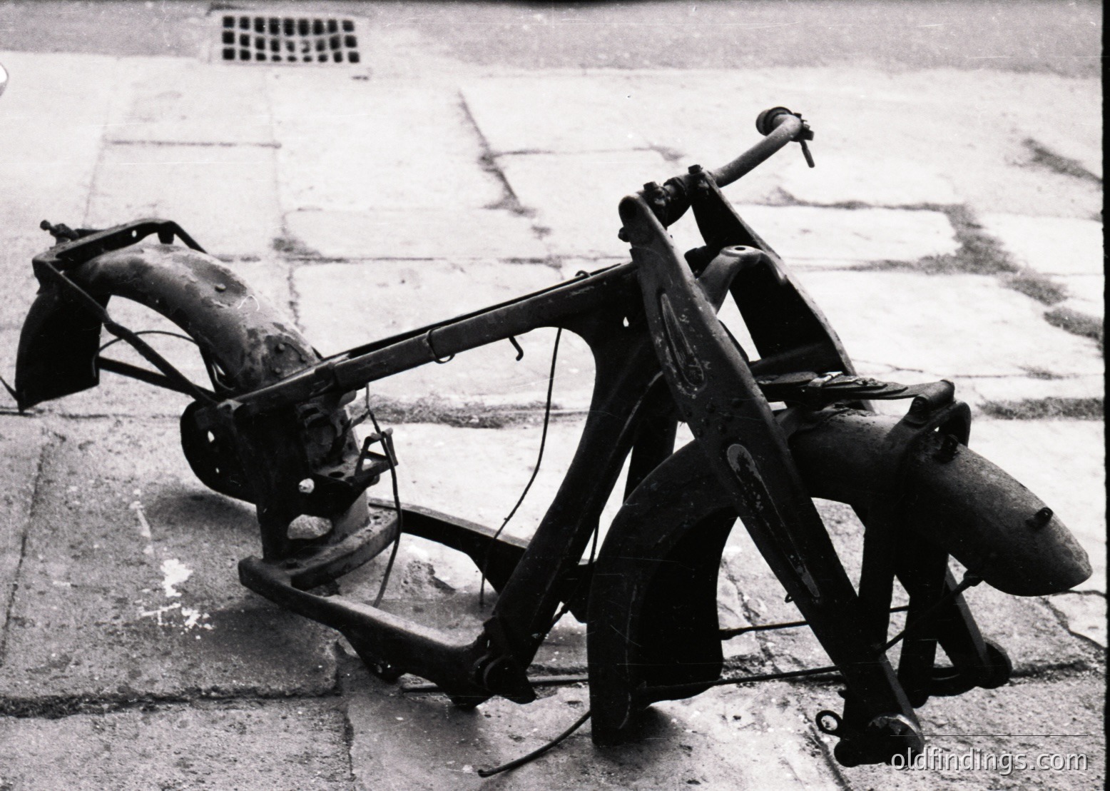 Vintage motorcycle frame with sidecar, likely mid-20th century. Rust and wear indicate prolonged outdoor exposure. Frame features classic tubular steel construction with visible chain drive and rear drum brake. Sidecar includes a simple bench seat and storage compartment.
