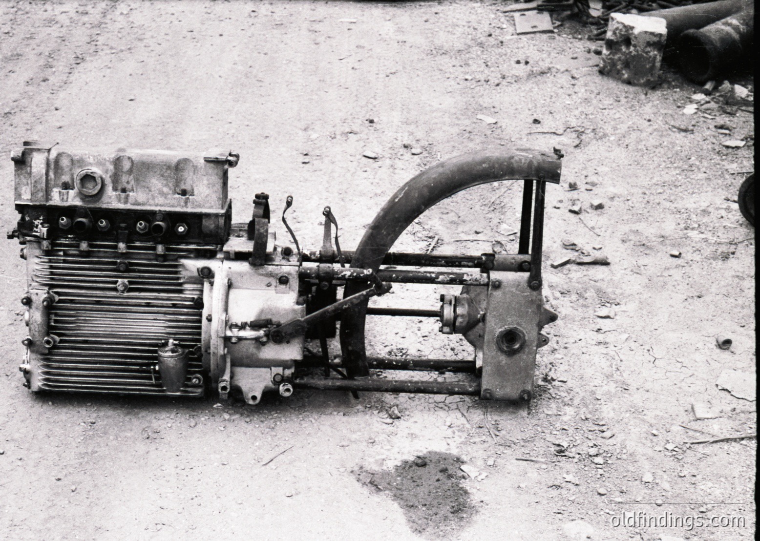 Vintage industrial engine with radiator fins, hand crank, and exposed mechanical components, likely mid-20th century. Rust and wear suggest prolonged outdoor use in a workshop or field setting.