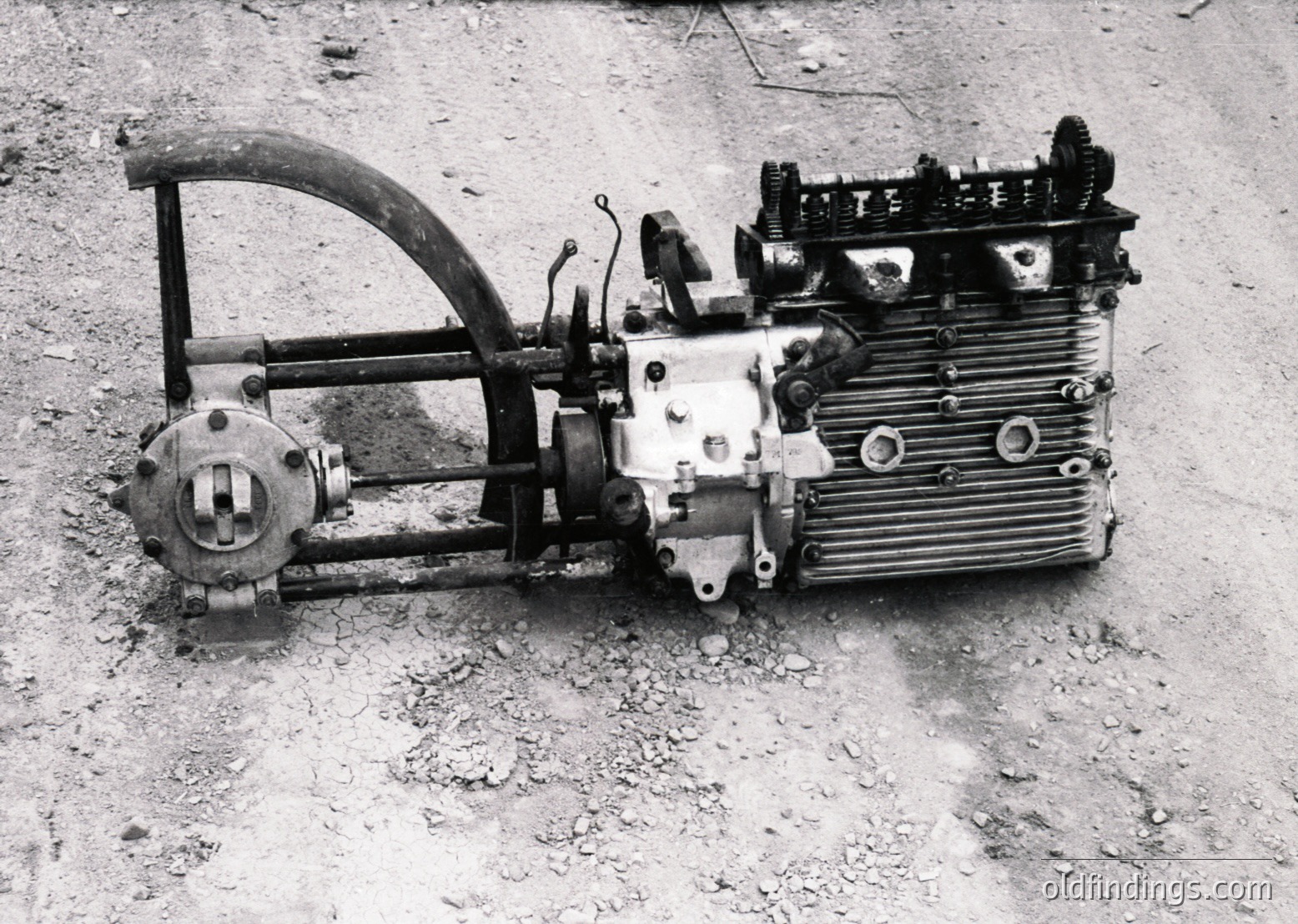 Vintage industrial engine with exposed inline cylinders, likely a diesel or steam-powered unit, mounted on a metal frame with a curved lever. Rust and wear suggest mid-20th century agricultural or construction use.