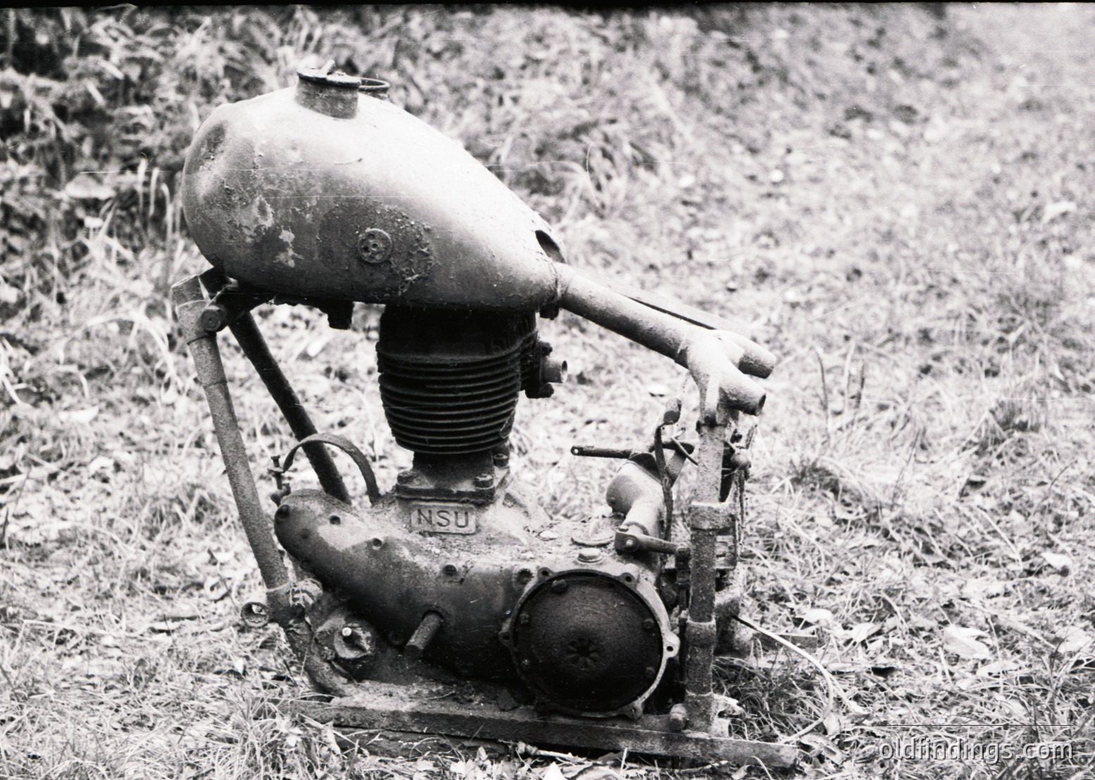 Vintage NSU two-stroke motorcycle engine, likely mid-20th century, displayed outdoors on grass. Rust and wear indicate prolonged outdoor exposure. Classic cylinder head and carburetor visible.