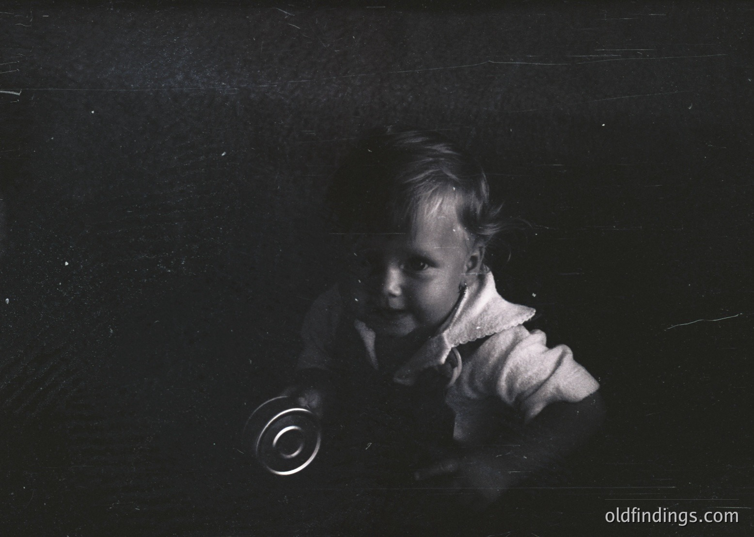 Black-and-white portrait of a young child in mid-19th to early 20th century attire, seated indoors with a vinyl record on floor. High-contrast lighting emphasizes texture of clothing and record grooves. Evokes early phonograph era.