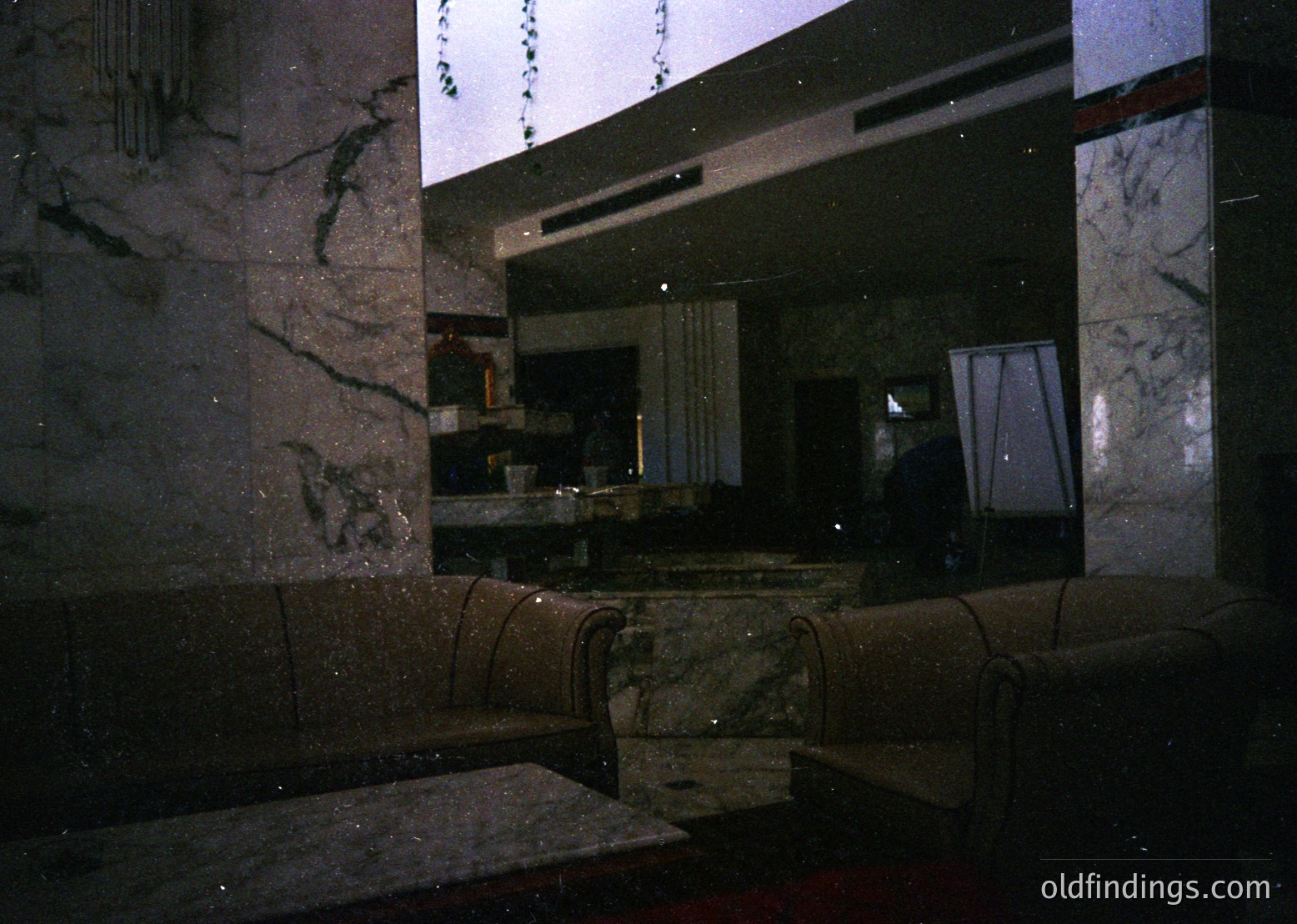 Marble-clad interior with geometric precision, featuring sleek countertops and built-in seating. Reflective surfaces capture a dimly lit kitchen area with a single candlelit dish. Mid-century modern design with clean lines and polished stone. Likely a 1960s–1970s residential or hotel space.
