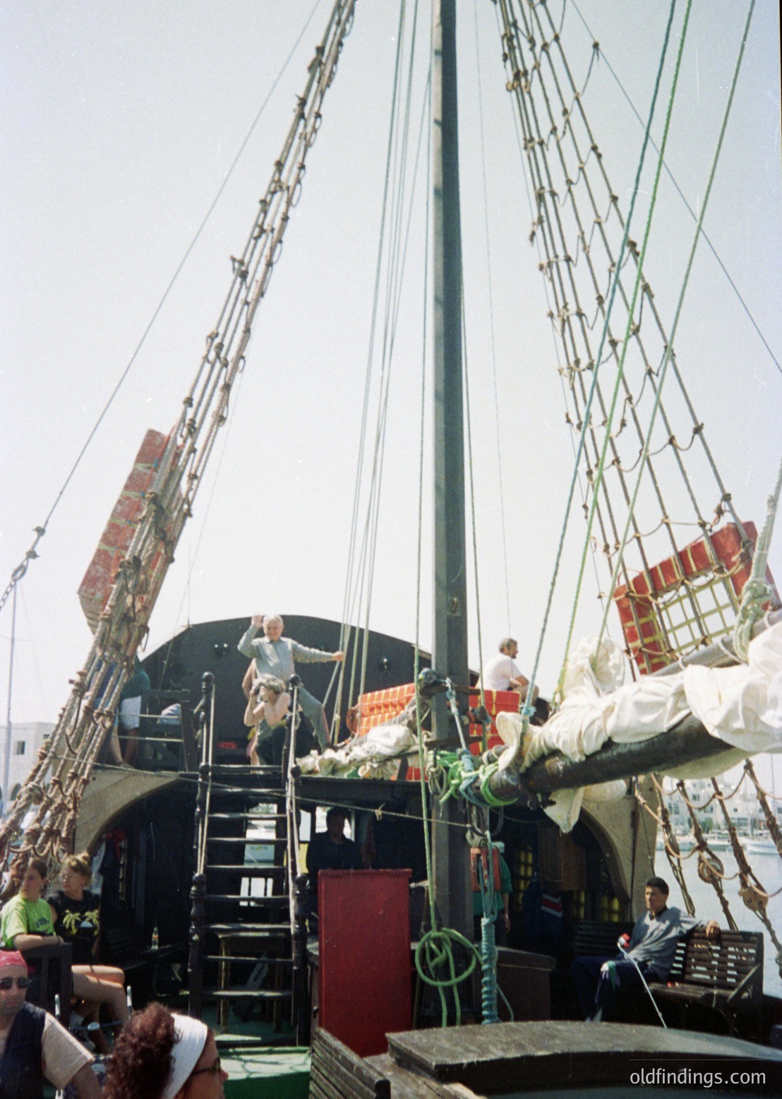 Reproduction of a 17th–18th century sailing ship deck, likely for maritime education or film. Crew in period attire climbs rigging and navigates wooden ladders. Crowd below observes, suggesting a public demonstration or event.