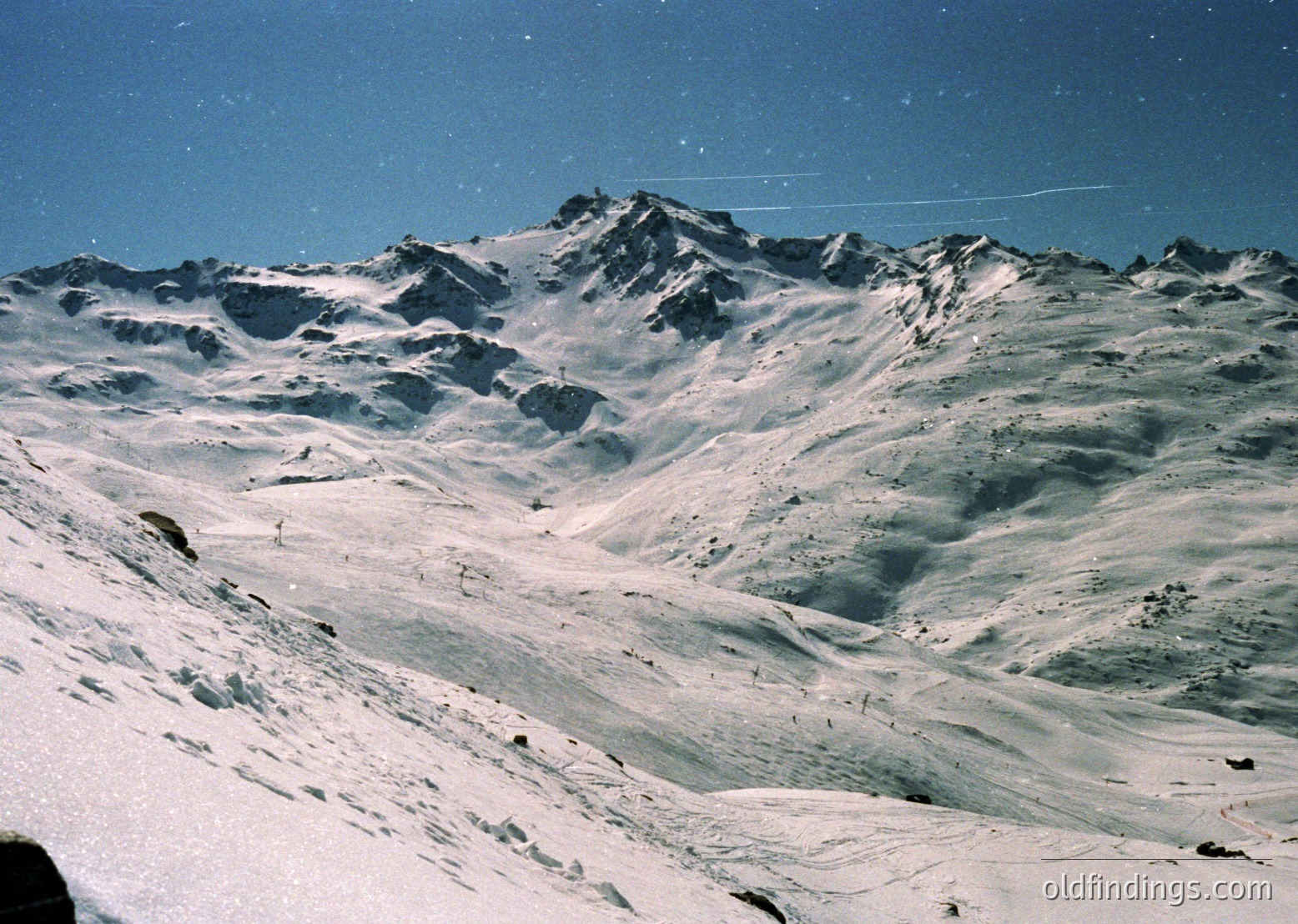 Snow-covered alpine peaks with jagged ridges under clear skies, likely European Alps. Dramatic lighting and texture highlight glacial formations and rocky outcrops. *(Note: The vintage color tone suggests a mid-late 20th-century photo, likely from a travel or adventure context.)*