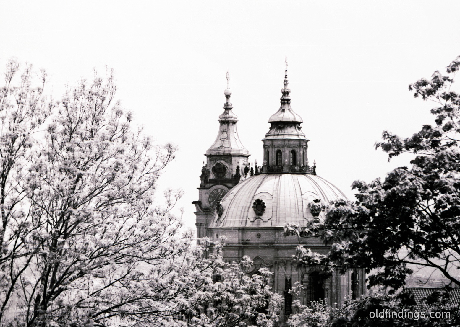 Baroque-style church dome with twin spires framed by leafless trees, suggesting winter or early spring. Ornate facade features decorative carvings and a central emblem. Likely European, 18th-century architecture. Ideal for historical research or vintage-inspired design references.