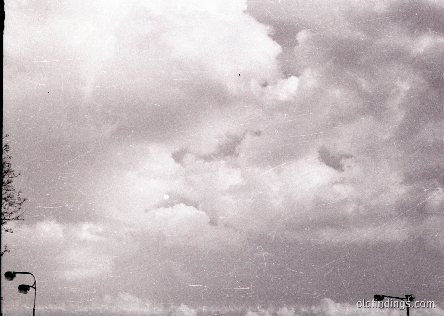 Vintage black-and-white aerial view of dense cloud cover with faint contrails crisscrossing sky. Partial urban landscape visible below, including streetlights and tree silhouettes. Likely mid-20th century aviation or meteorological documentation.