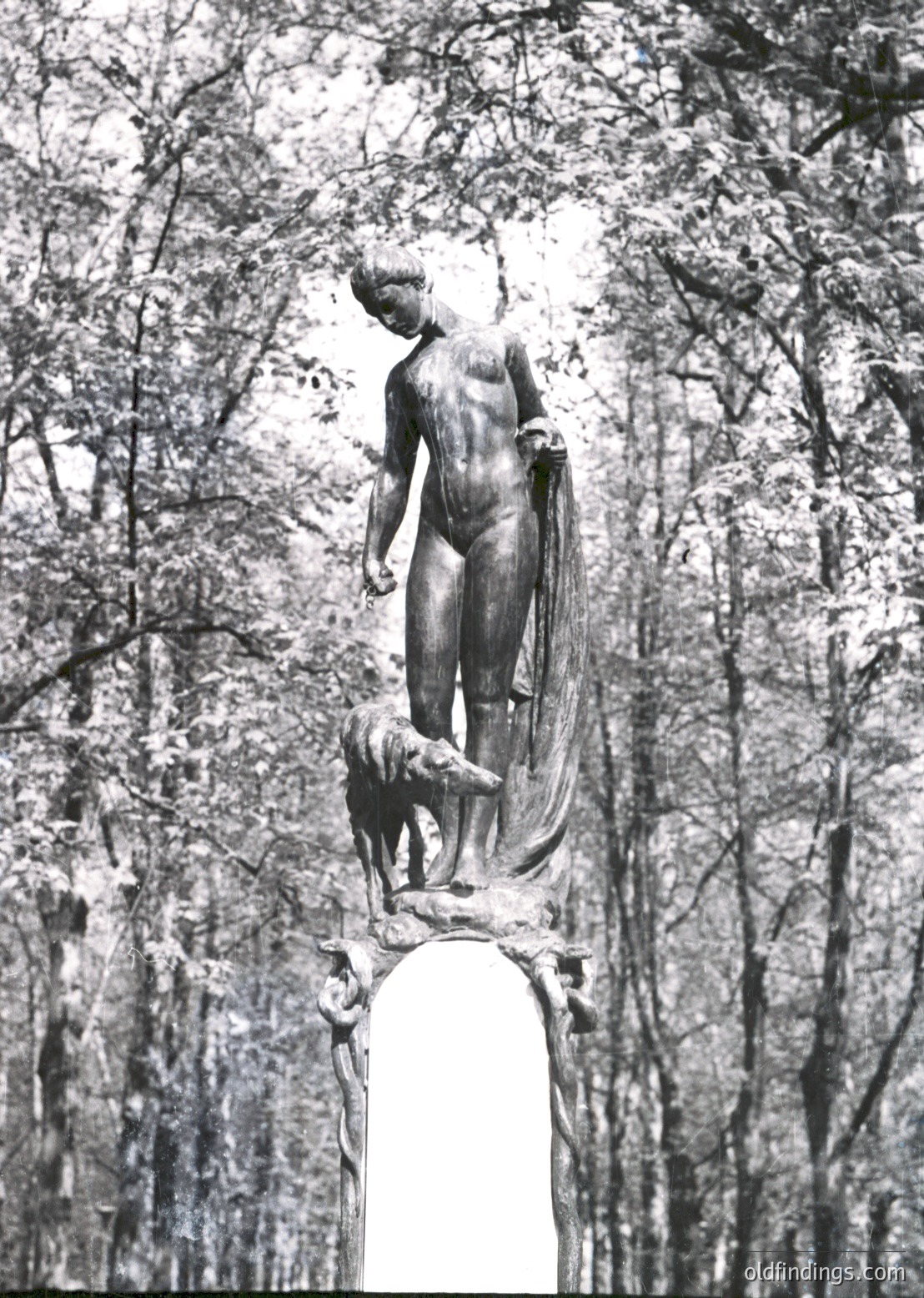Bronze statue of a robed figure holding a crouching dog atop a pedestal, set in a wooded area. Likely a 20th-century public monument, possibly or . The serene forest backdrop suggests a commemorative or symbolic purpose.