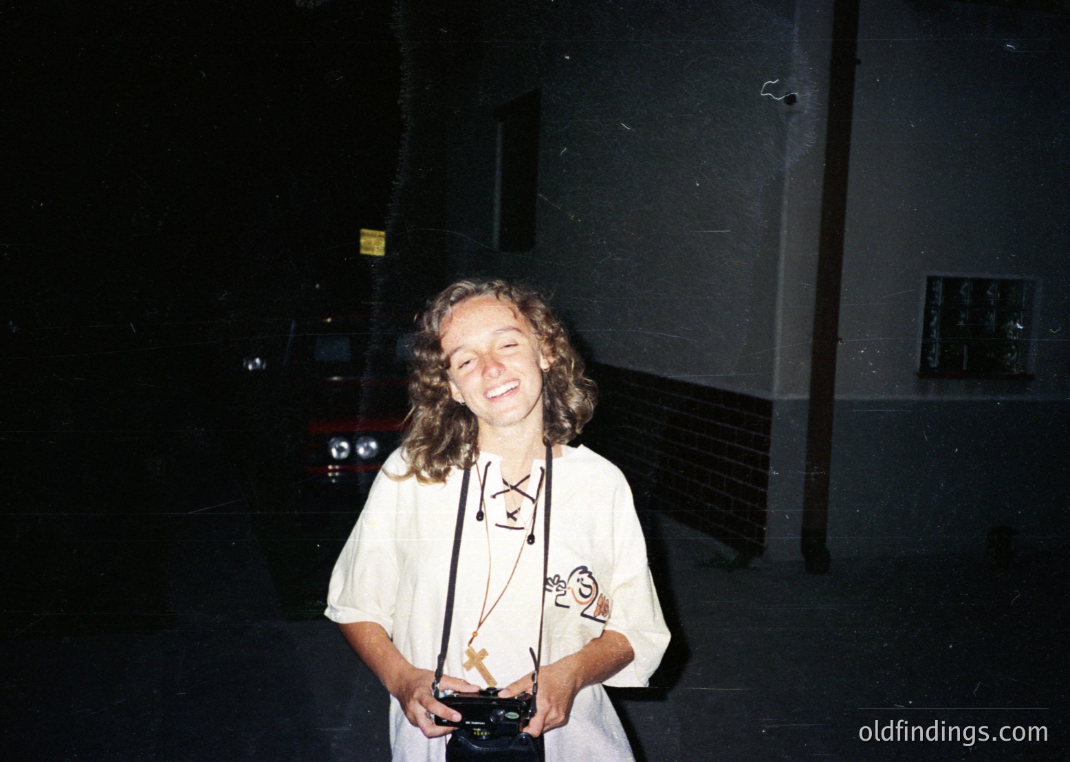 Vintage candid of a person in a 1970s-style lanyard with a lanyard badge and a small trophy, likely from an event or competition. Indoor setting with dim lighting and a blurred background featuring a vehicle.