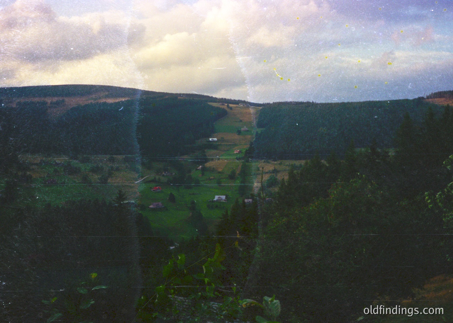 Vintage glass-paneled view of rural valley with layered hills, scattered farmhouses, and dense forest. Distorted perspective from aged glass reveals autumnal greens and earthy tones. Likely European countryside, 20th-century residential architecture.