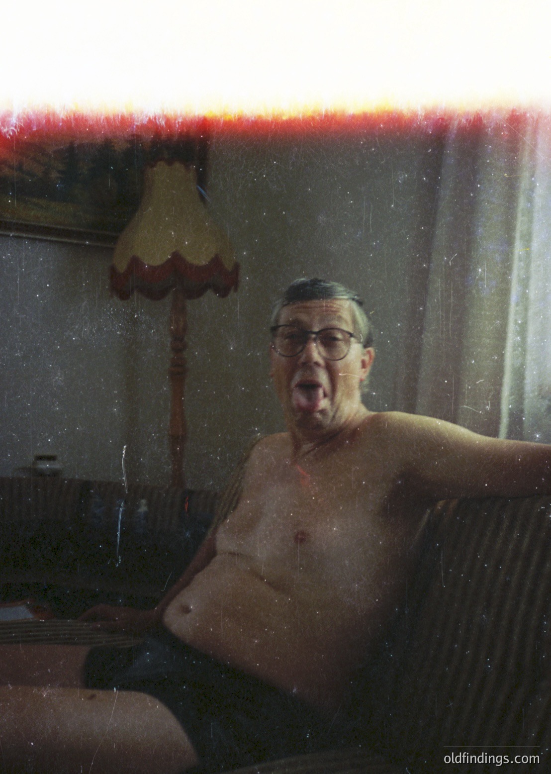 Vintage black-and-white photo of a middle-aged man in a bathtub, mid-laugh, with a red-lensed filter. Wooden bathtub, vintage lamp with red shade, and blurred background suggest mid-20th-century domestic setting.