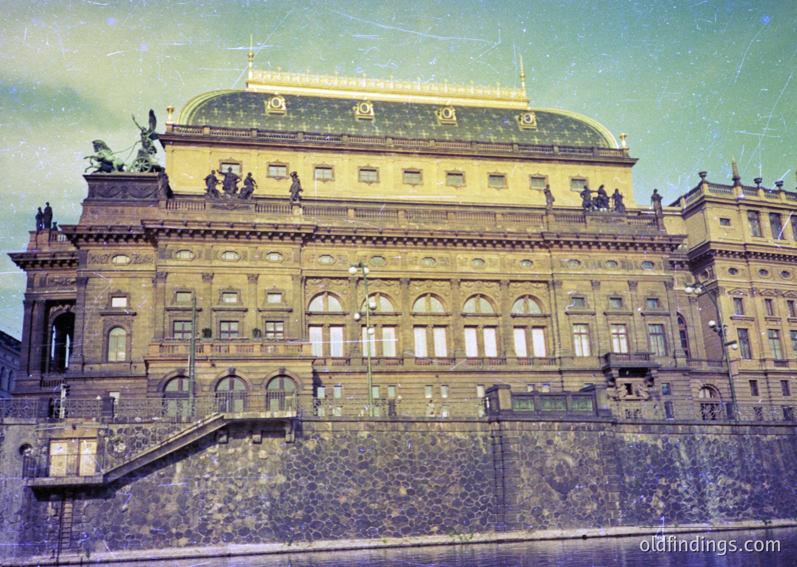 Grand neoclassical theater façade with ornate bronze statues, arched windows, and a domed roof. Architectural details suggest early-to-mid 20th century European design. #