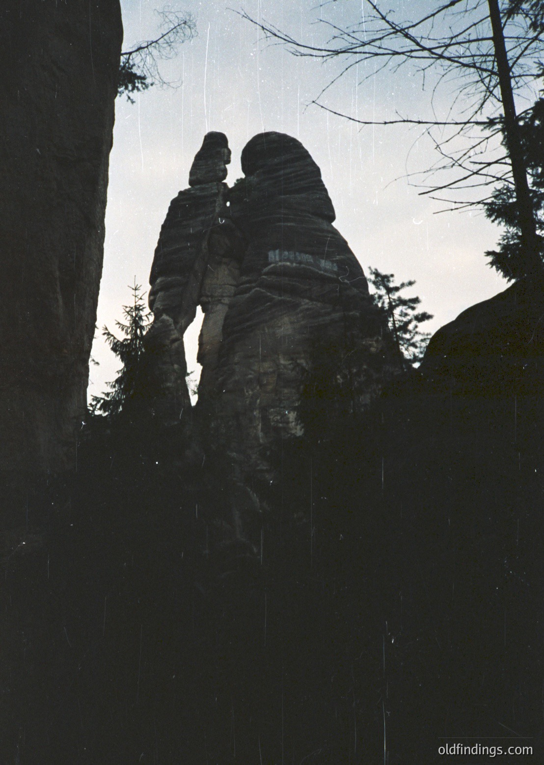 Silhouetted figures embracing atop layered sandstone rock formations in a rainstorm, likely Sächsische Schweiz (Germany). Dramatic vertical composition highlights erosion patterns and misty atmosphere. ächsischeSchweiz