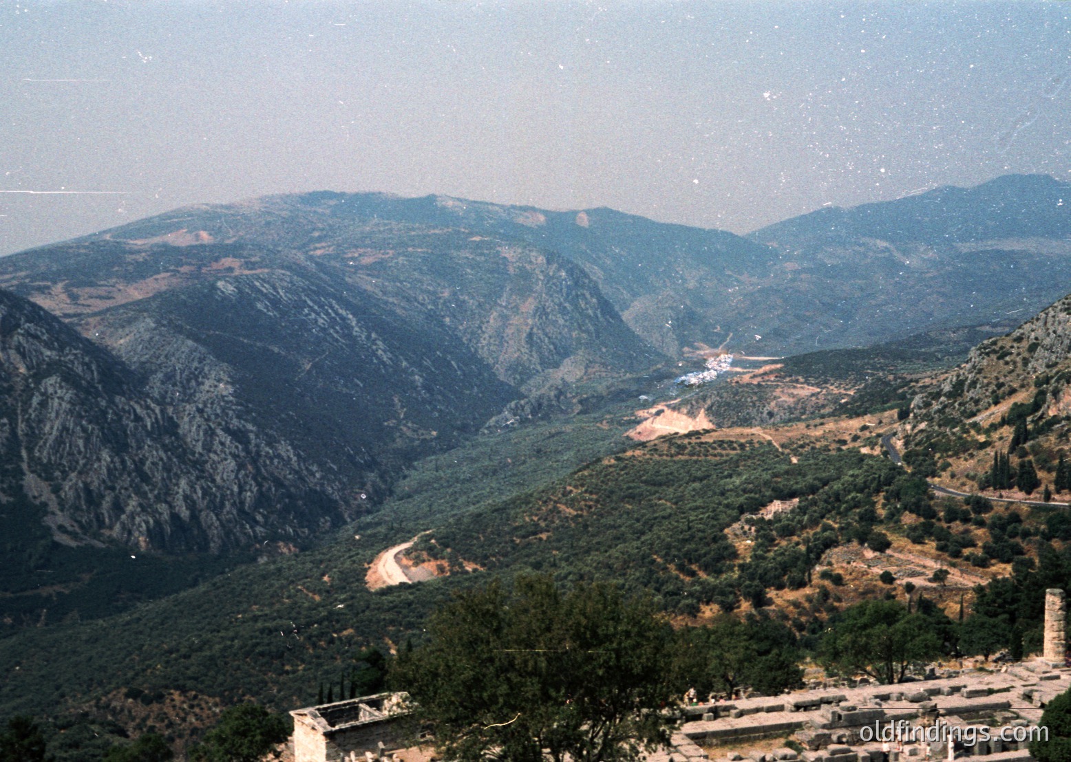 Vast mountainous valley with winding road and scattered vegetation, likely Mediterranean or Balkan region. Distinctive terraced slopes and sparse development suggest rural or undeveloped terrain. Vibrant greens contrast with rocky ridges under clear skies.