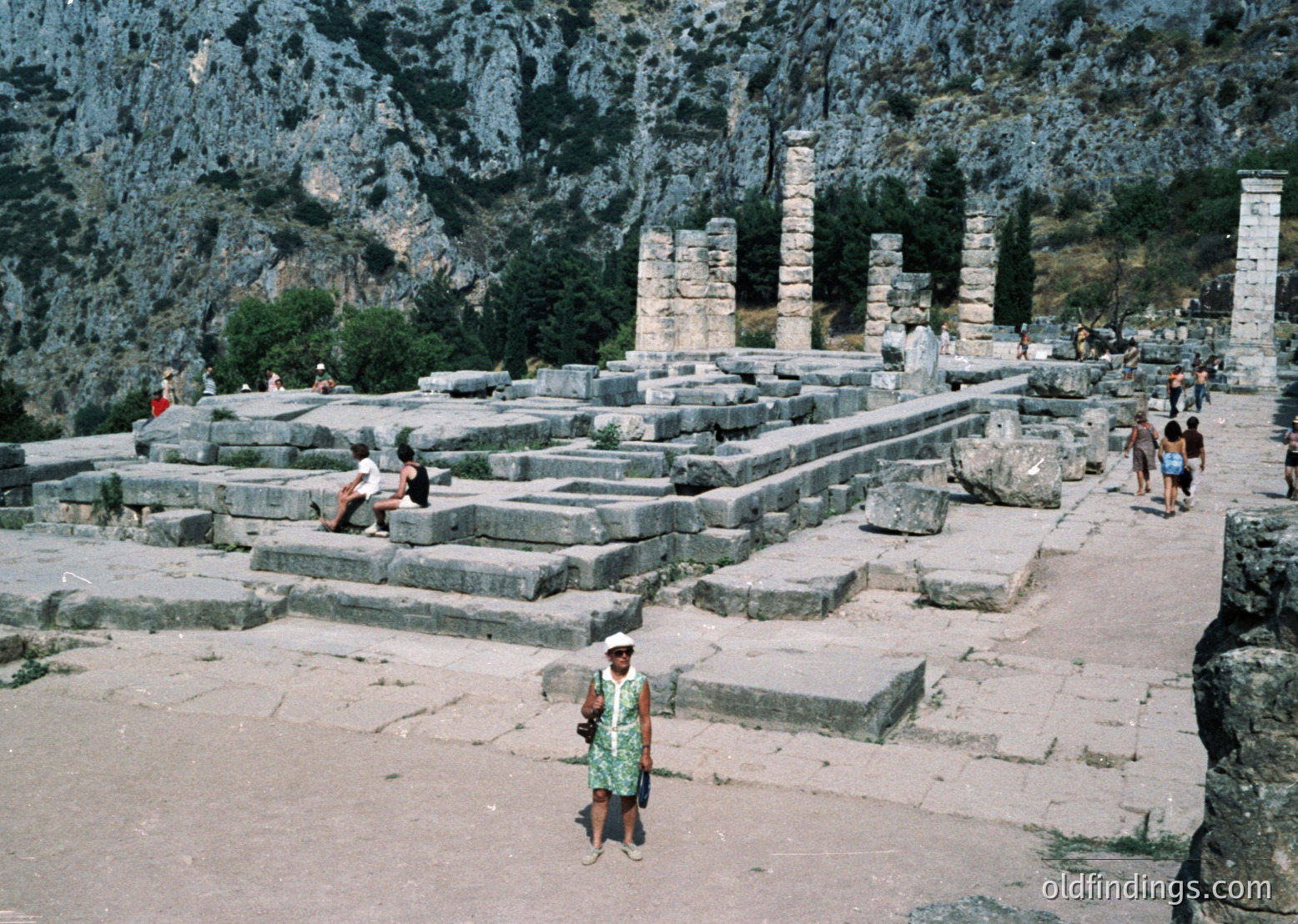 Ancient Hellenistic ruins featuring Doric columns and stone platforms in a mountainous setting. Likely the Temple of Dionysus at Thasos, Greece, dating to 4th–3rd century BCE. Visitors explore the archaeological site amid rugged cliffs.