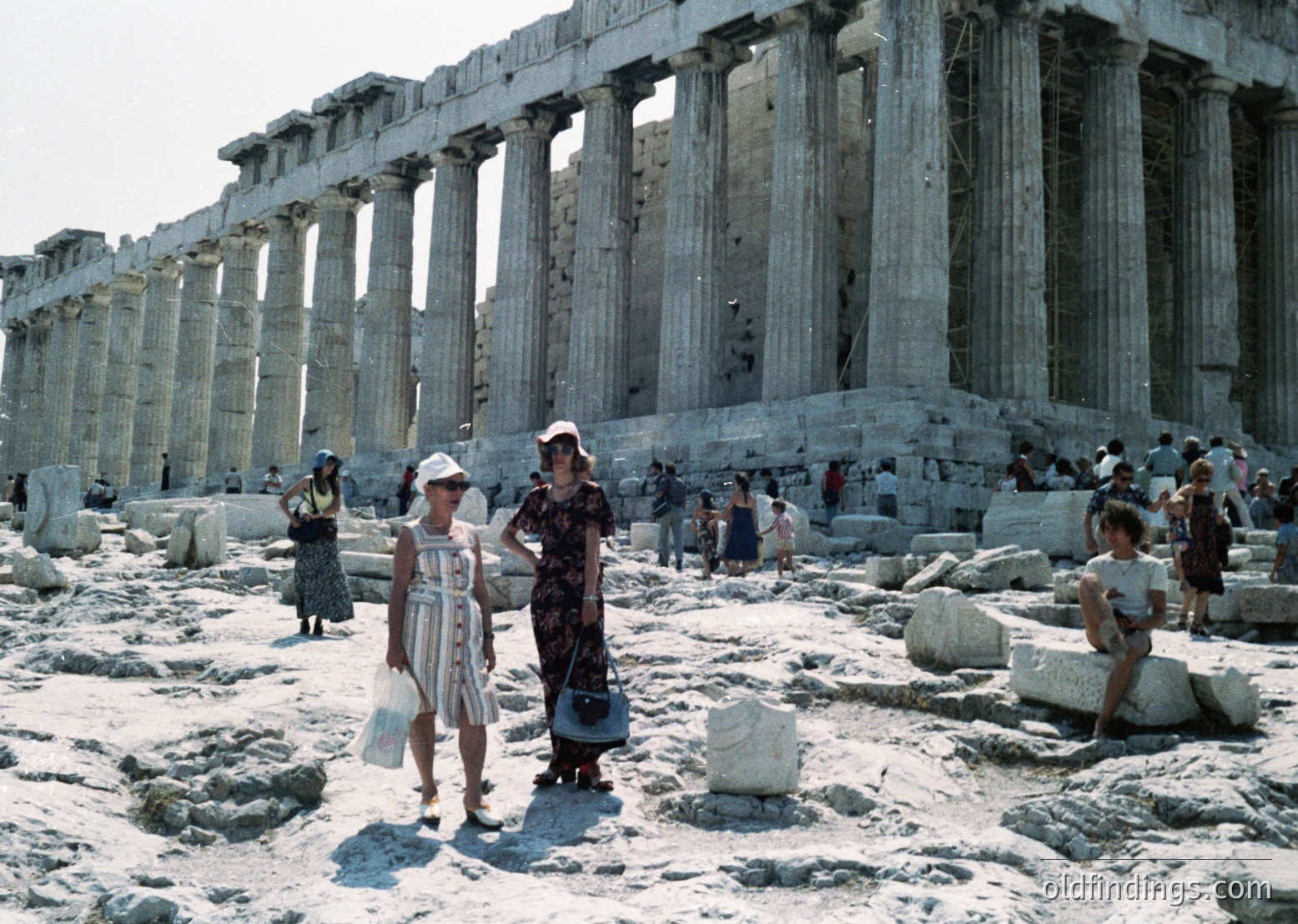 Classic 5th-century BCE Greek Doric architecture of the Parthenon ruins in Athens, Greece. Mid-20th century (1950s–1960s) tourists in summer attire explore the ancient site. Distinctive striped dress and straw hat in foreground.