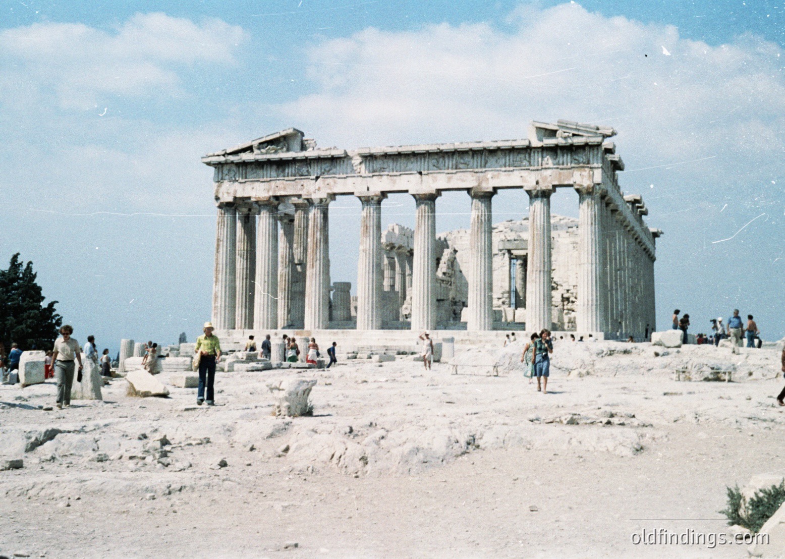 The Erechtheion’s iconic Doric and Ionic columns dominate this 1960s-era photo, captured on the Acropolis in Athens, Greece. Visitors explore the ancient temple’s ruins, with scattered stone fragments and a clear sky overhead. The photograph’s vintage sepia tone highlights mid-century tourism.