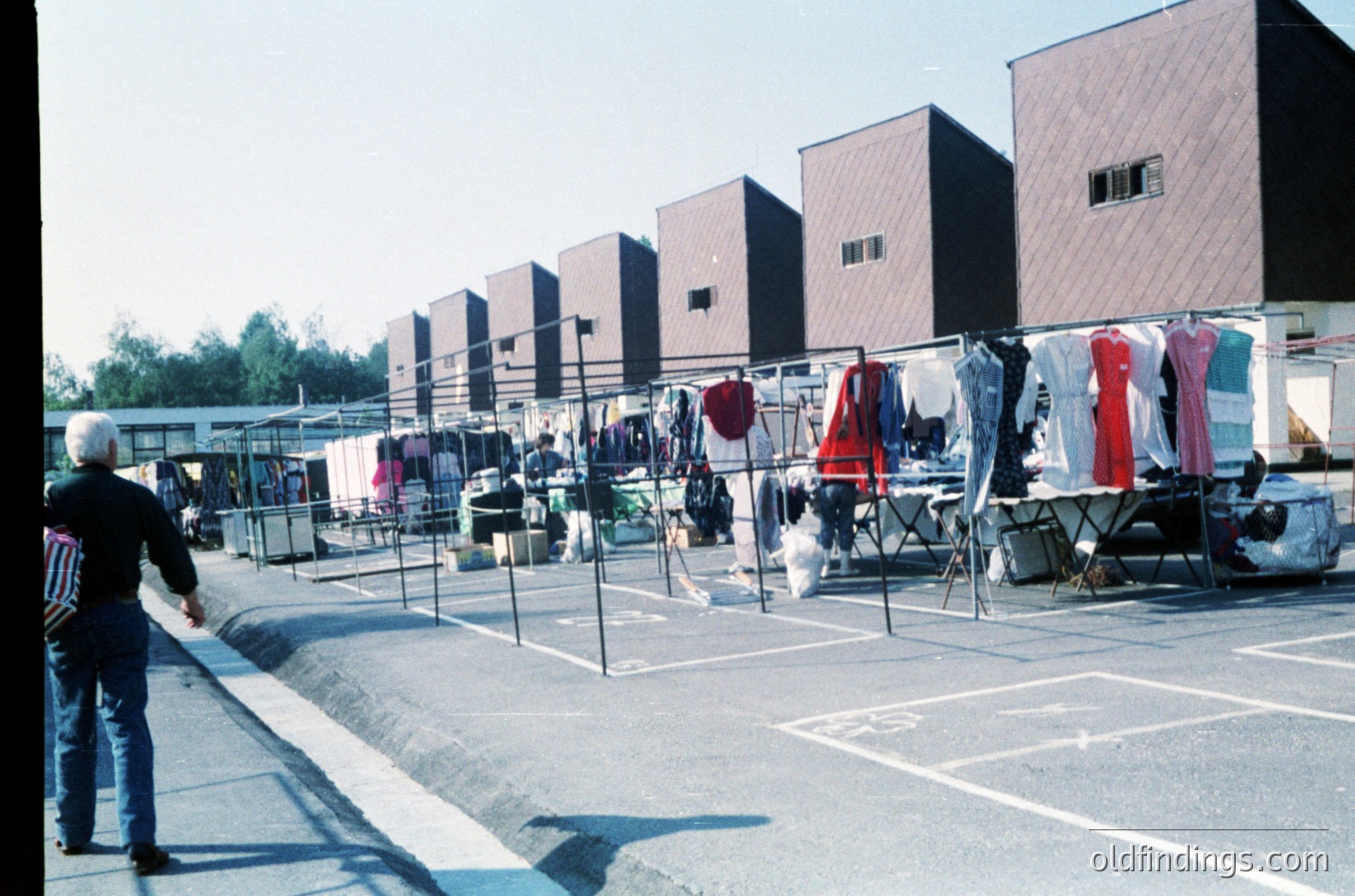 Communal rooftop laundry area with concrete slabs, metal racks, and drying clothes in a Soviet-era apartment block. A man in a striped shirt and cap walks toward the foreground. Brutalist architecture with flat roofs and minimalist design. Likely Eastern Europe, 1970s–1980s.