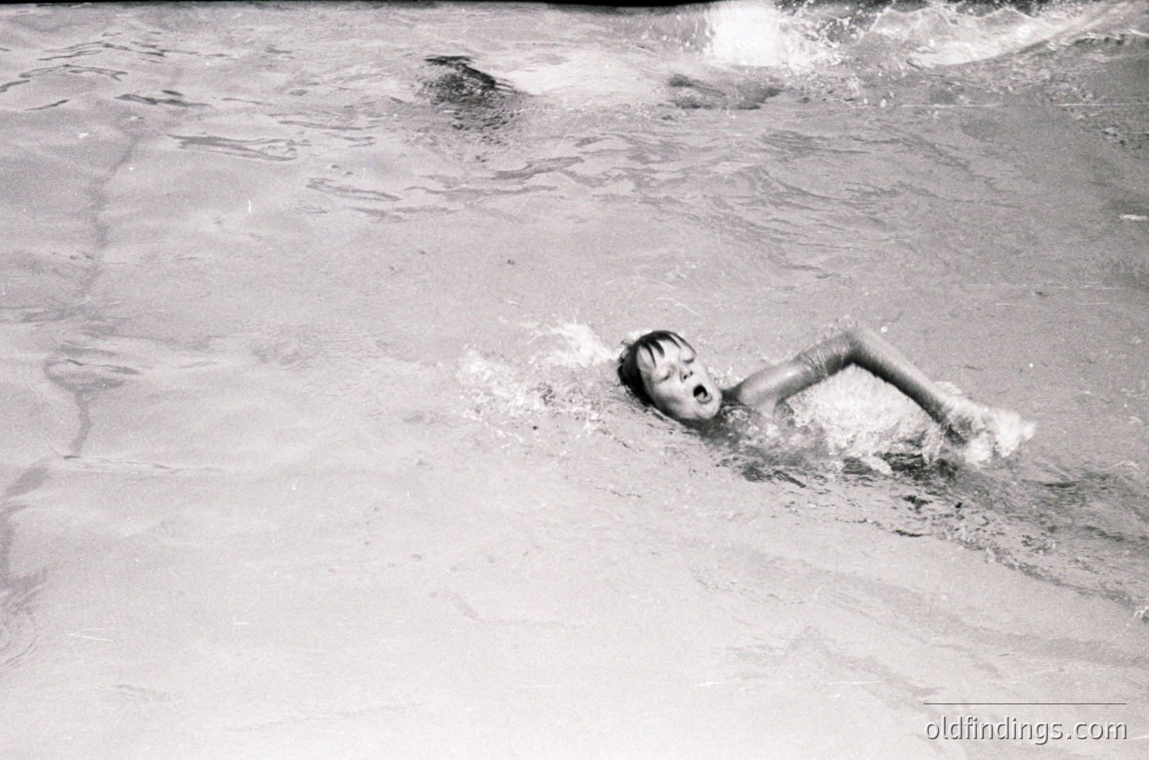 Black-and-white shot of a child mid-dive into shallow water, arms extended forward. Dynamic composition captures motion and youthful energy. Likely mid-20th century based on style.