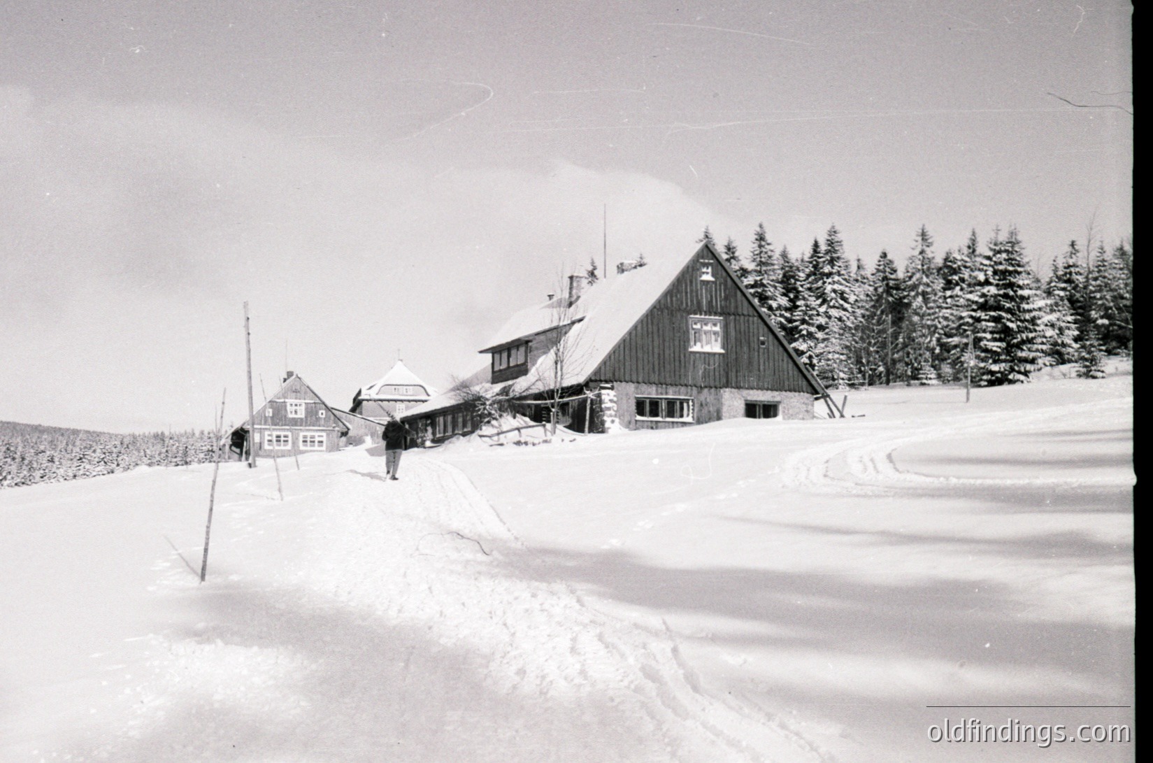 Mid-20th century alpine lodge complex blanketed in snow, surrounded by evergreen forest. Timber-framed buildings with peaked roofs, one labeled "Pension" in German script. Snow-covered slopes and tracks suggest winter recreation. Likely European alpine region, 1950s–1970s.