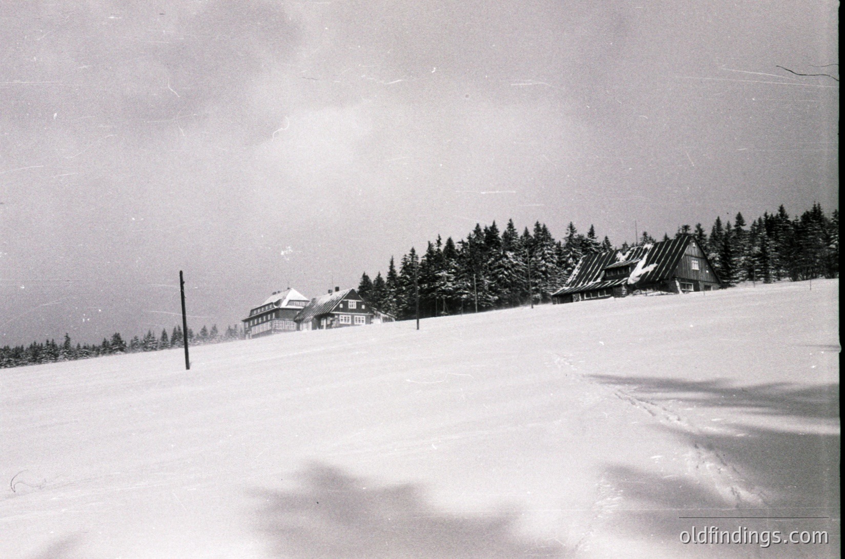 Mid-century alpine resort complex nestled in snow-covered forest, likely European. Multi-story wooden chalet-style buildings with sloped roofs, surrounded by dense evergreen trees. Snowy landscape suggests winter sports or skiing. Vintage black-and-white photo, 1950s-1960s era.