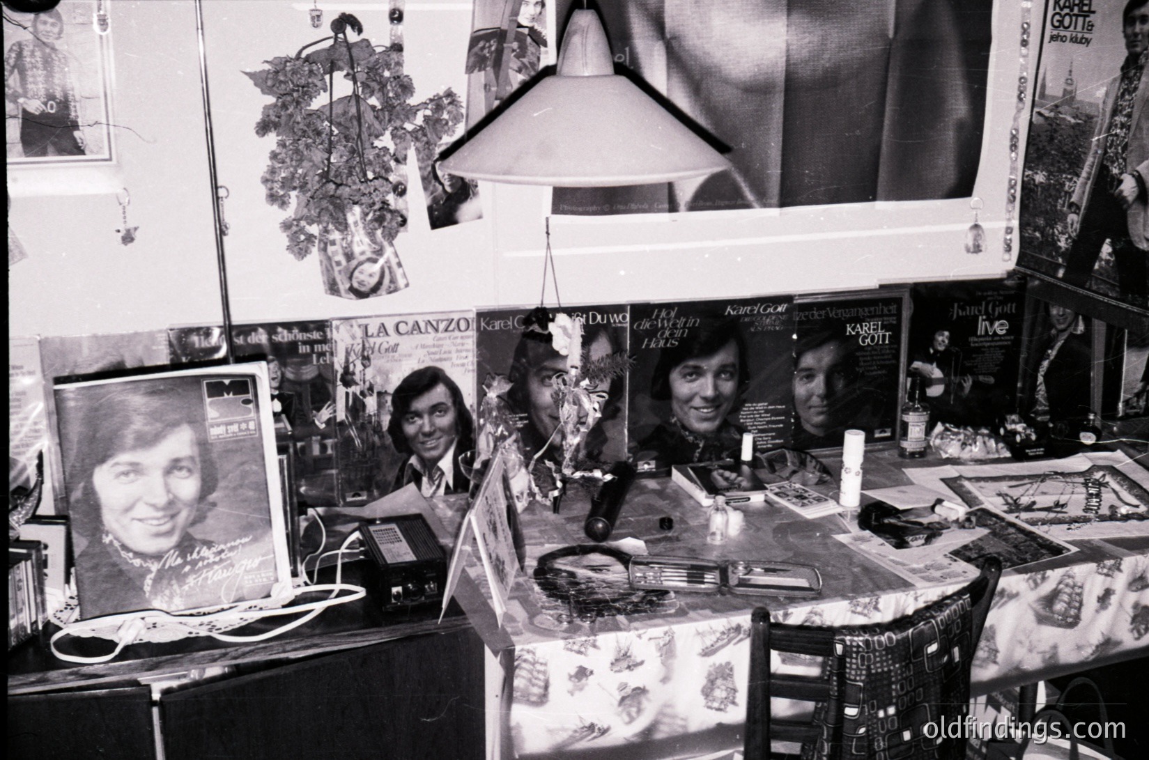 Vintage 1970s music memorabilia display featuring album covers, posters, and a framed portrait. Visible artists include Karel Gott, La Canzo, and others. Decorated with garlands and a hanging light fixture. Likely a record shop or private collection.