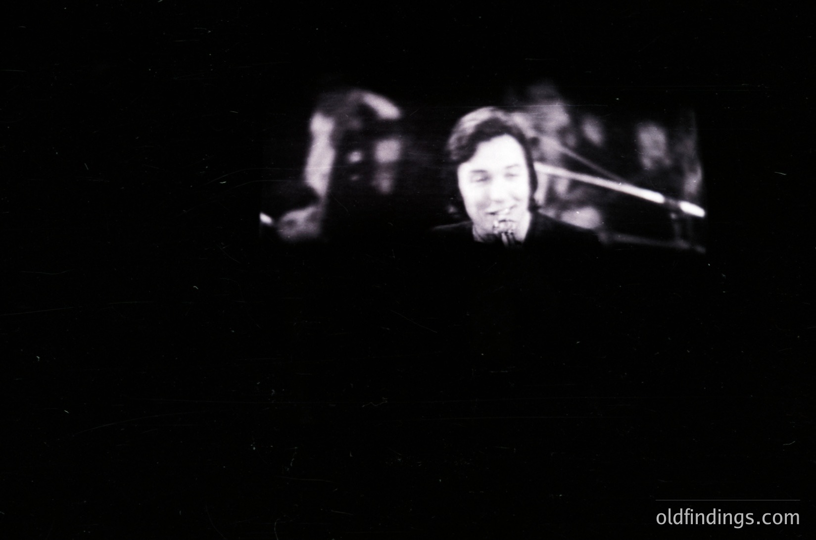 Blurred black-and-white close-up of a saxophonist performing live, captured with shallow depth of focus. The musician’s focused expression and instrument detail suggest a mid-20th-century jazz or blues setting. Vintage grain and lighting emphasize mood over clarity.
