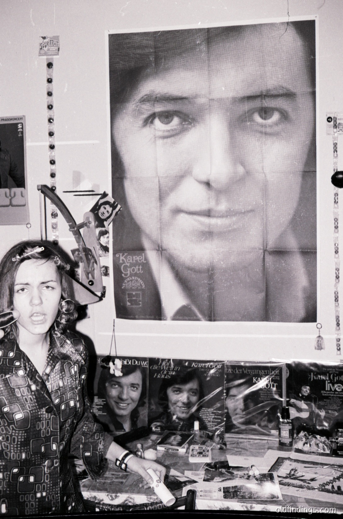 Vintage collage featuring a large portrait of Karel Gott (1970s Czech pop icon) alongside a smaller, fragmented image of a woman in a patterned dress. The scene includes cut-out magazine clippings, a toy bow, and a toy bow-and-arrow. Likely a nostalgic or artistic homage to mid-century European pop culture.