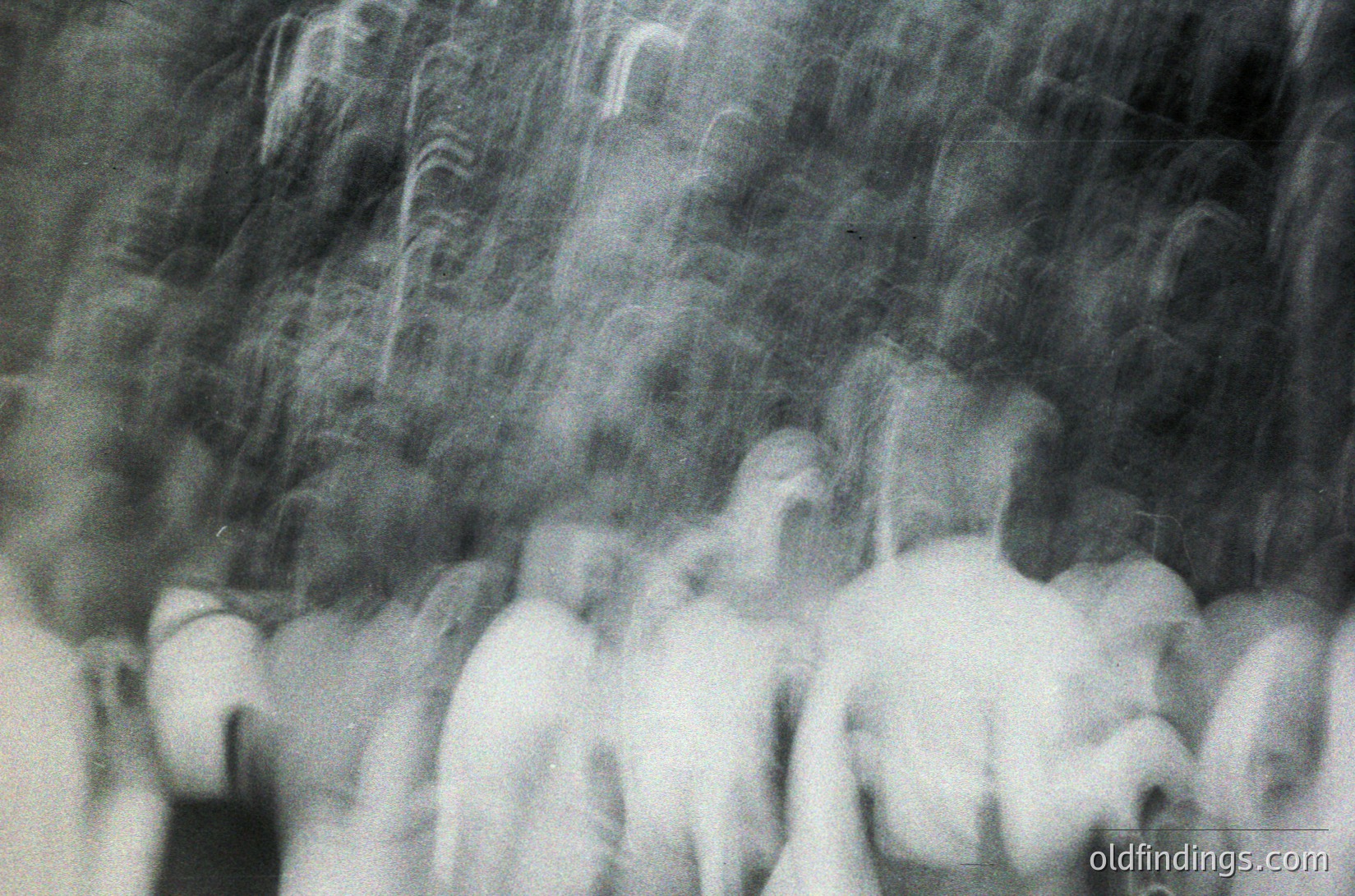 Blurred monochrome street scene with indistinct figures in motion, likely from a handheld camera. Motion blur suggests rapid movement or long exposure. Potential urban setting with indistinct architecture in background. Style reminiscent of 1960s–1970s street photography.