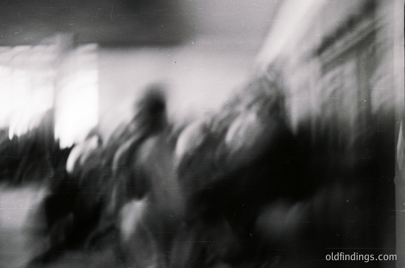Blurred monochrome shot capturing motion blur of a crowd in an indoor setting, likely a public event or gathering. Soft focus obscures faces, emphasizing dynamic energy. Possible 1960s–1980s era based on grain and lighting.