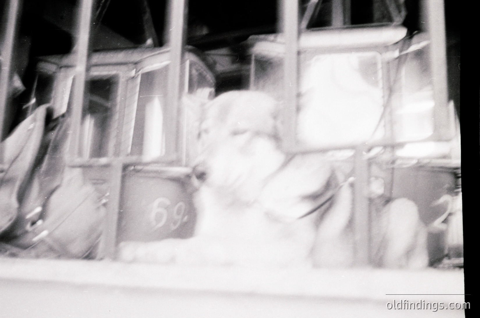 Blurred black-and-white shot of a vintage telephone booth () with a seated figure inside, likely from the mid-20th century. Reflections and motion blur obscure details, emphasizing nostalgia and urban anonymity. Potential use for retro design or historical research.