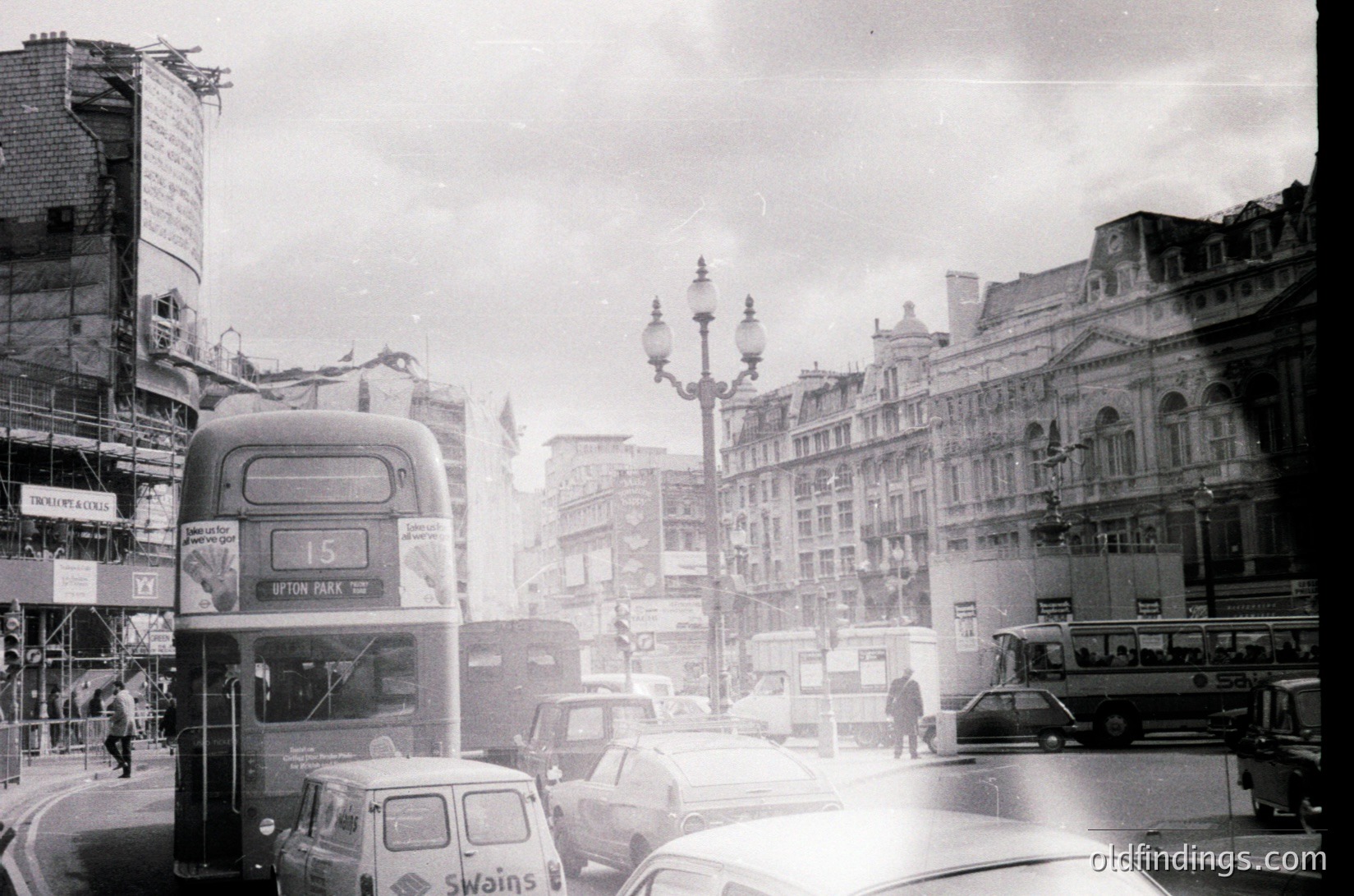 Classic mid-20th century London street scene with iconic double-decker bus (route 15) and vintage cars. Edwardian-era buildings flank a busy intersection, blending historic architecture with mid-century urban life. Fog or mist obscures distant details, adding nostalgic atmosphere. Likely 1950s–1960s