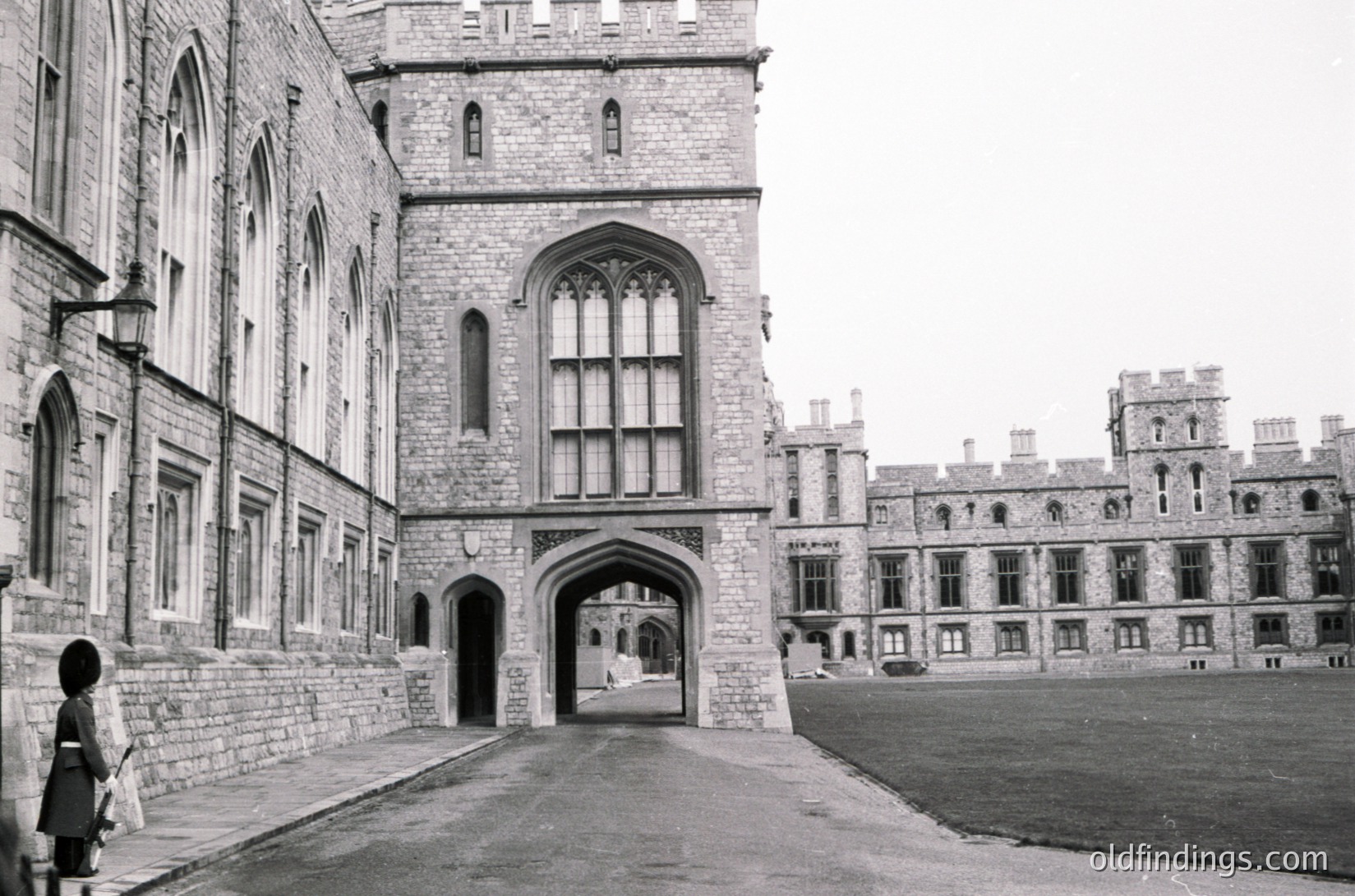 Gothic-style stone courtyard entrance with pointed arches, tall lancet windows, and buttresses. Mid-20th century institutional architecture, likely a university or historic building. Empty paved courtyard with minimal human presence.