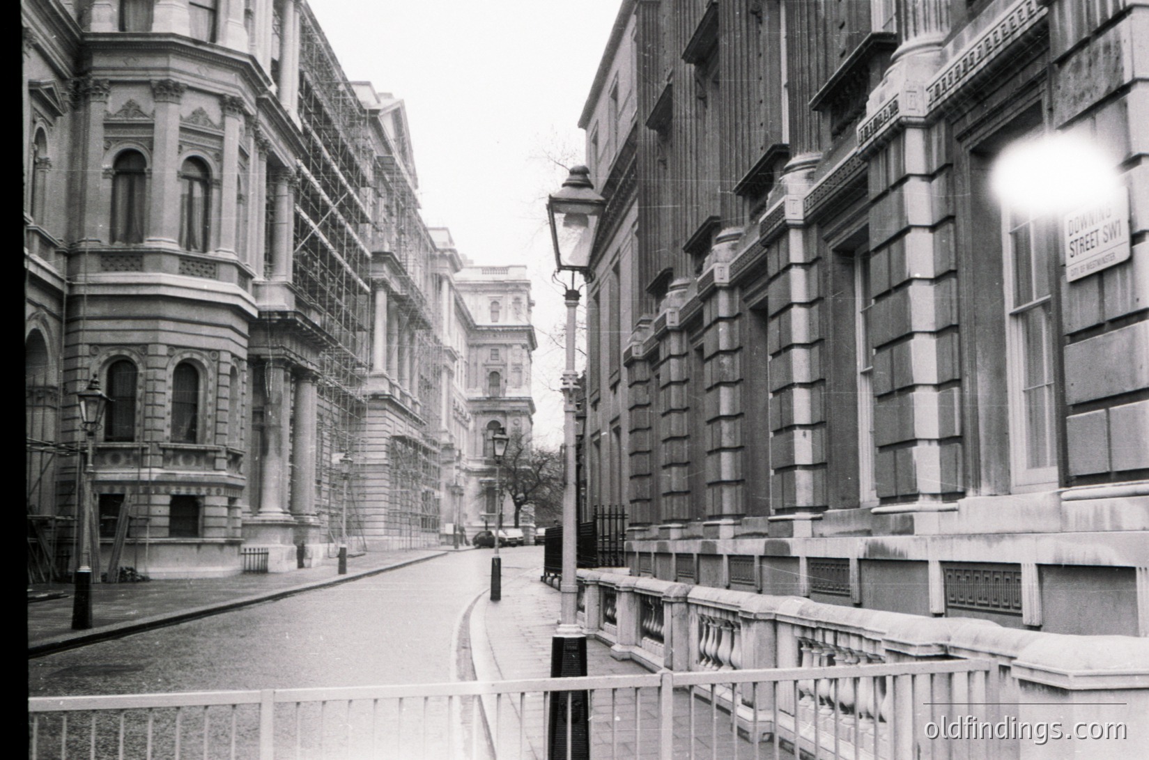 Classic early 20th-century London street view, showcasing Edwardian-era architecture. Symmetrical stone buildings with ornate balconies, wrought-iron railings, and street lamps line both sides. Narrow, slightly inclined street with minimal pedestrian activity.
