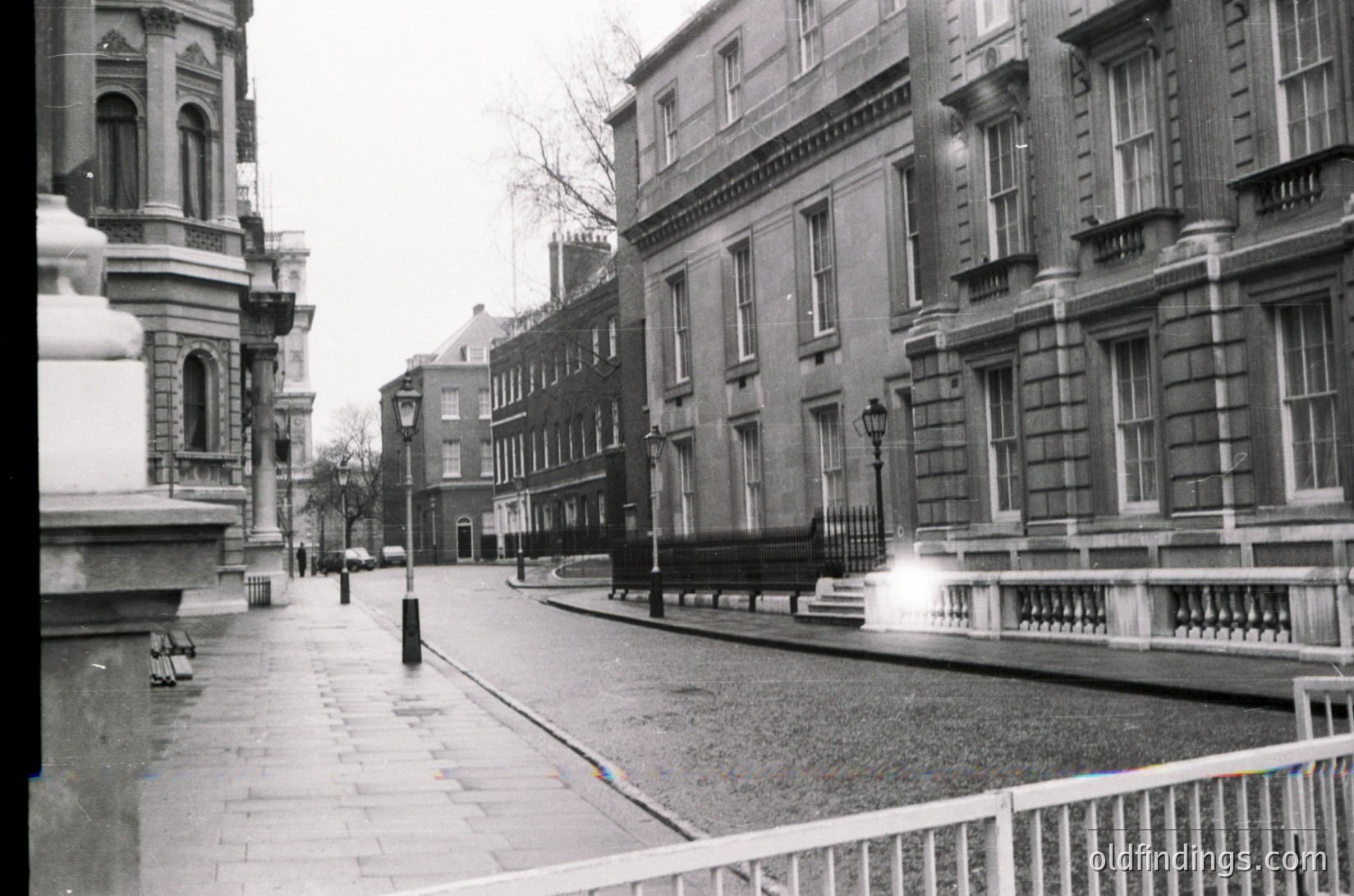 Neatly preserved mid-20th century urban street in classic European architecture. Symmetrical row of brick buildings with ornate facades, wrought-iron railings, and vintage street lamps. Empty pavement suggests early morning or off-peak hour.