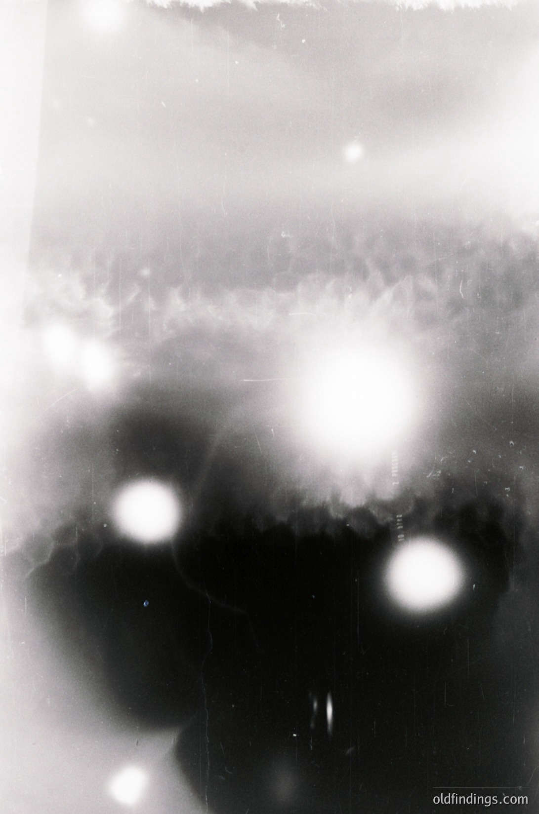 Vintage high-contrast black-and-white photo of abstract light reflections on a textured surface, likely glass or water. Circular bokeh patterns dominate the composition, suggesting a camera lens or underwater lens flare. Undefined shapes and streaks add depth. Potential use for moody, artistic stock or experimental photography references.