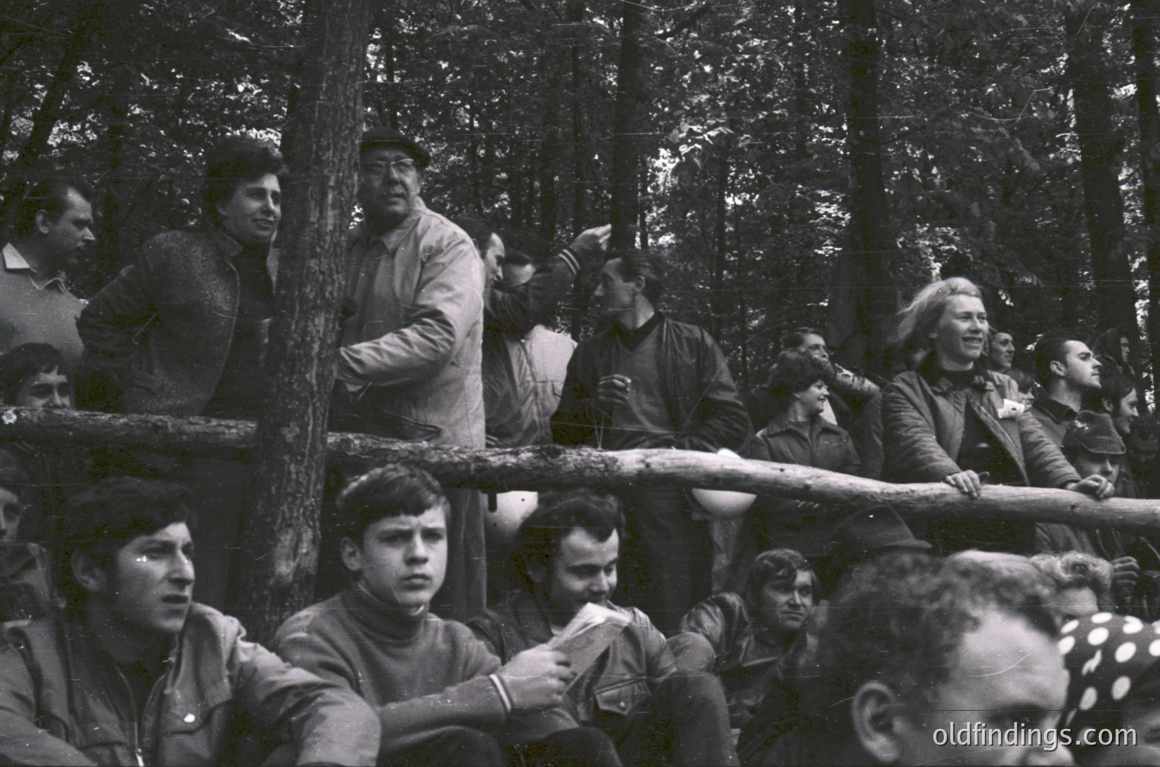 Group of men in military-style uniforms and caps gathered outdoors in a forested area, likely Eastern Bloc 1960s–70s. Uniforms feature patch pockets and shoulder insignia. Dense foliage and natural lighting suggest a rural or training camp setting.