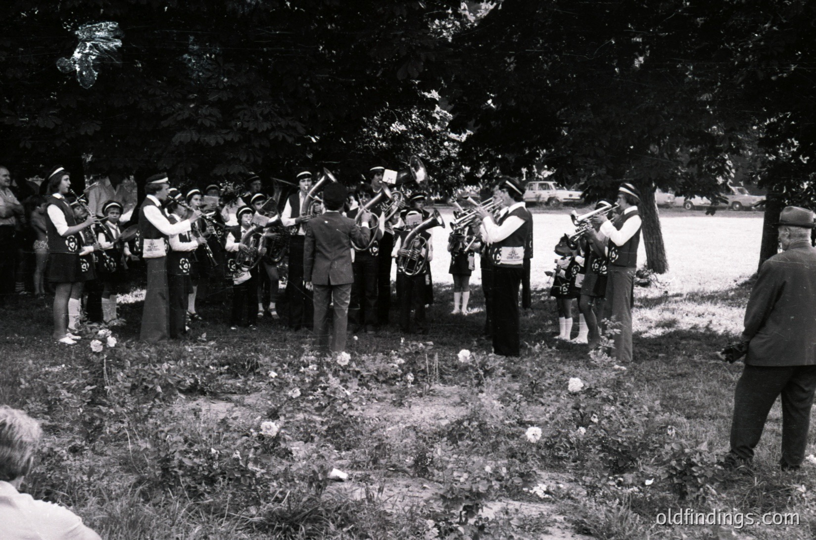 Group of musicians in outdoor setting playing brass instruments at a graveside ceremony, likely mid-20th century. Uniformed figures and floral arrangements suggest a formal memorial or funeral.