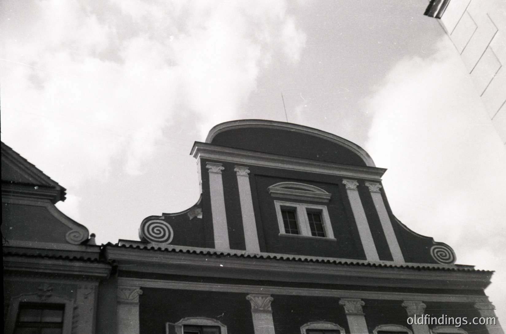 Neoclassical rooftop with decorative spiral motifs and cornice details, captured in black-and-white. Symmetrical windows and a curved pediment suggest 19th-century European architectural influence. Potential urban setting, likely for historical research or design references.