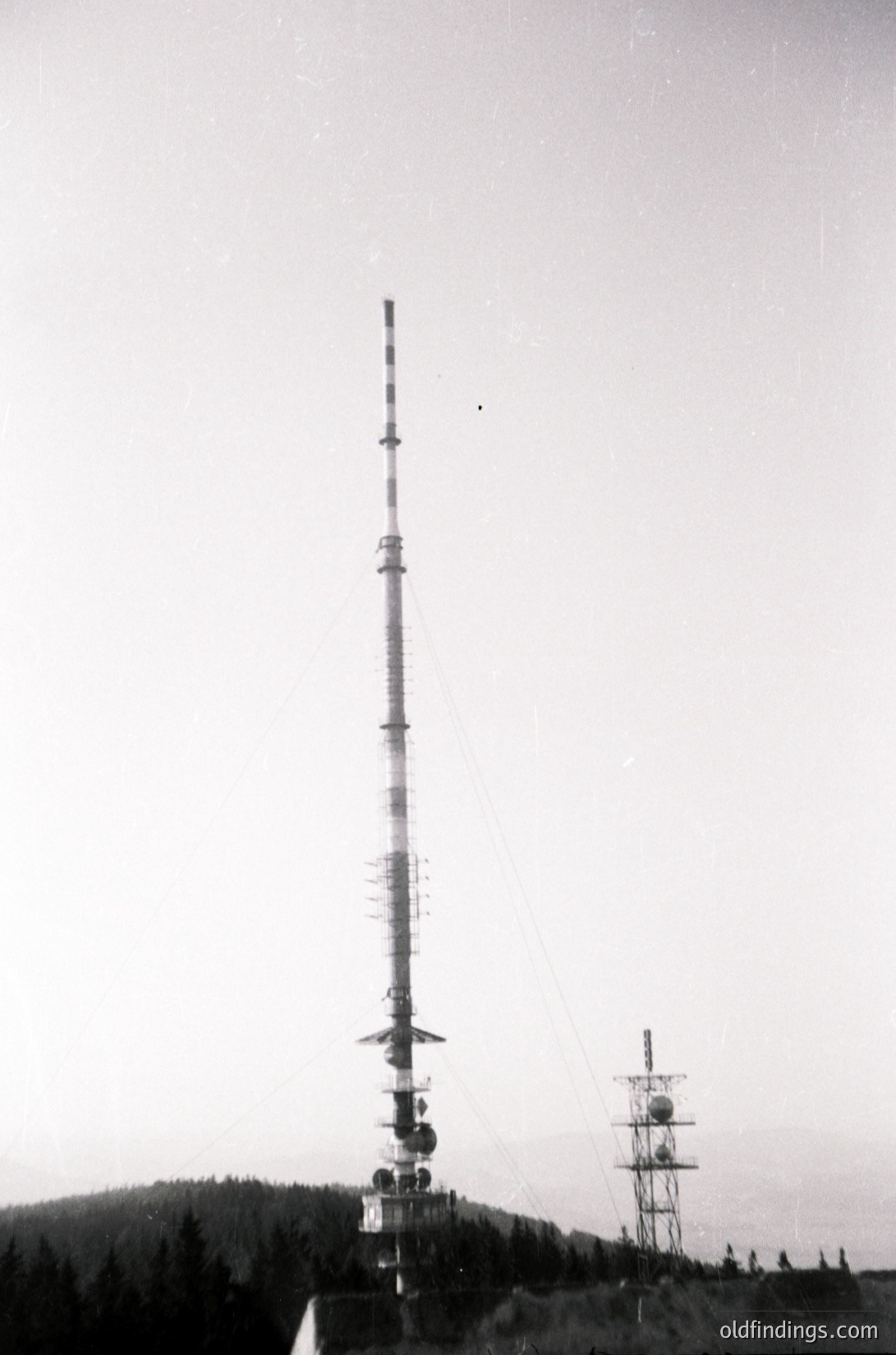 Mid-20th century communications tower with spherical antennas, set against forested hills. Likely a Cold War-era military or research facility.
