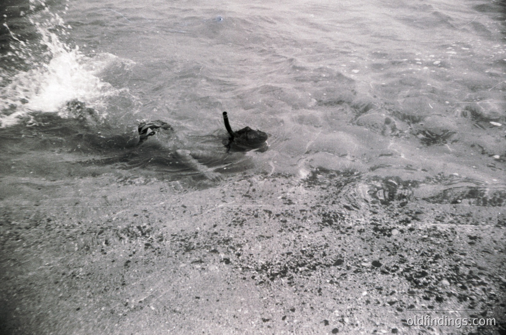 Black-and-white shot of a vintage military tank partially submerged in churning water, likely during amphibious training or testing. Distinctive turret and tracks visible.