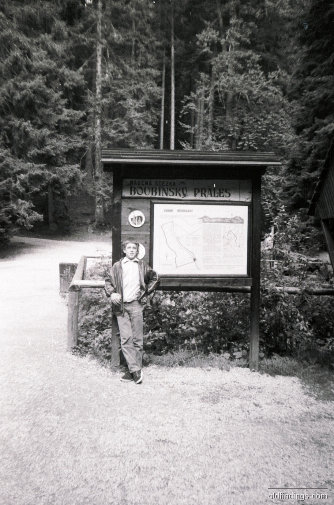 Vintage black-and-white photo of a man posing beside a wooden informational board in a forested area. The sign reads *"Boubinský Prašivý"* with a map and hiking route details, suggesting a Czech Alpine trail. Mid-20th century attire and signage indicate or . Ideal for historical hiking or outdoor research. ýPrašivý