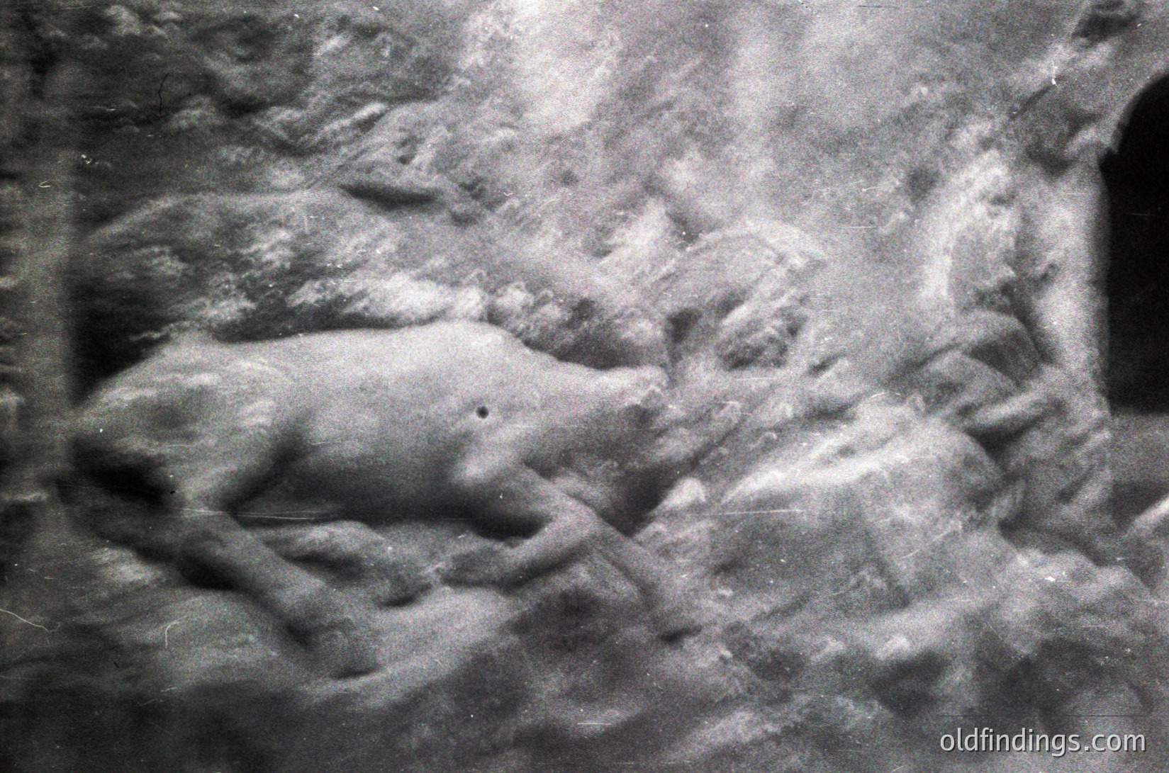 Close-up of a **stone relief sculpture** depicting a reclining figure, likely a historical or mythological subject. The intricate carving shows detailed musculature and drapery, suggesting classical or ancient influences. Possible **Greek/Roman** origin or inspired by such art.