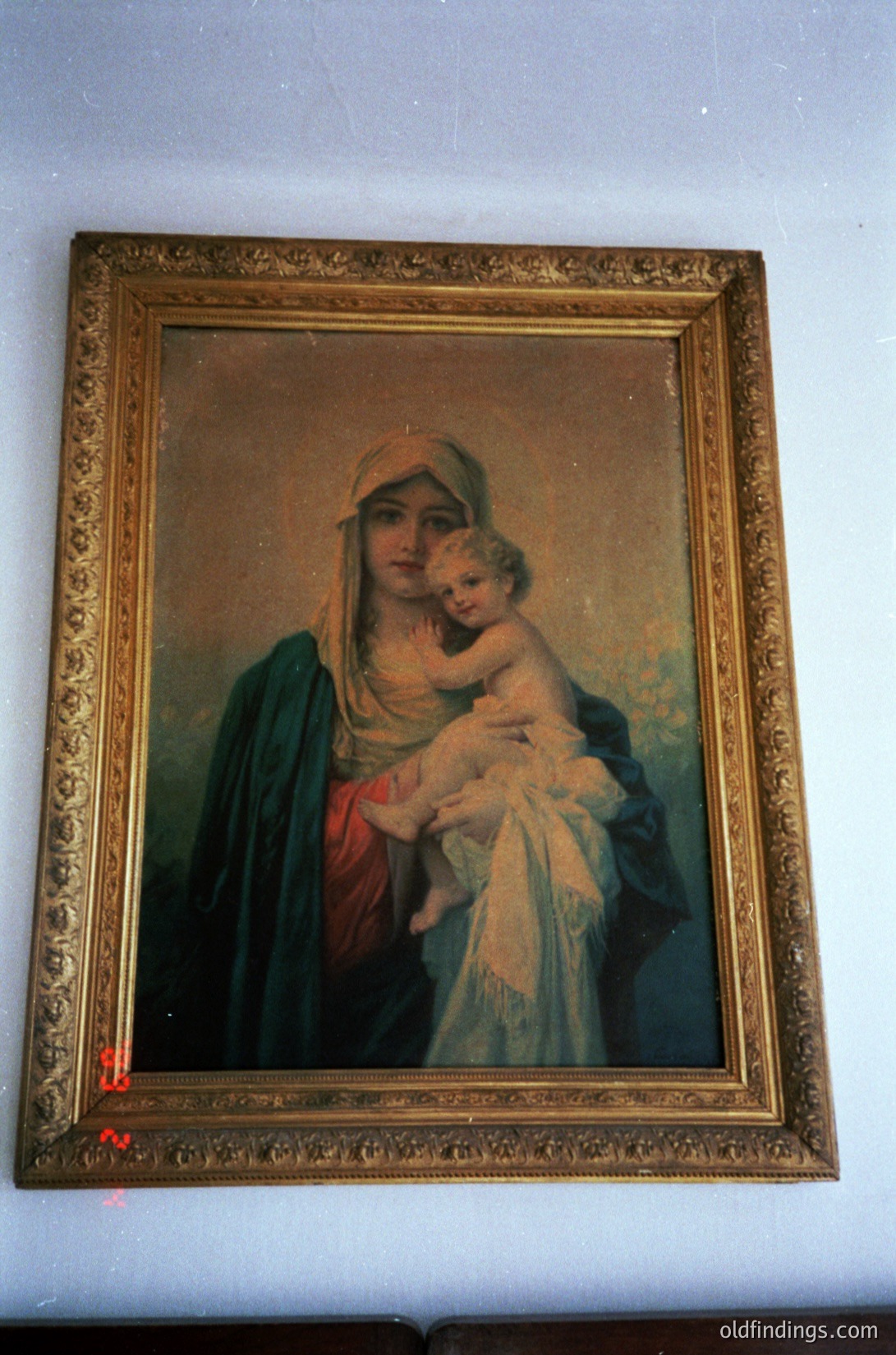 Religious portrait depicting the Virgin Mary cradling infant Jesus, framed in ornate gilded wood. Soft brushstrokes and muted tones suggest late 19th to early 20th century European religious art. Ideal for historical research on Christian iconography or vintage interior design.